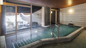 Una piscina interior moderna con paredes de vidrio transparente, techo de madera y suelo de baldosas.