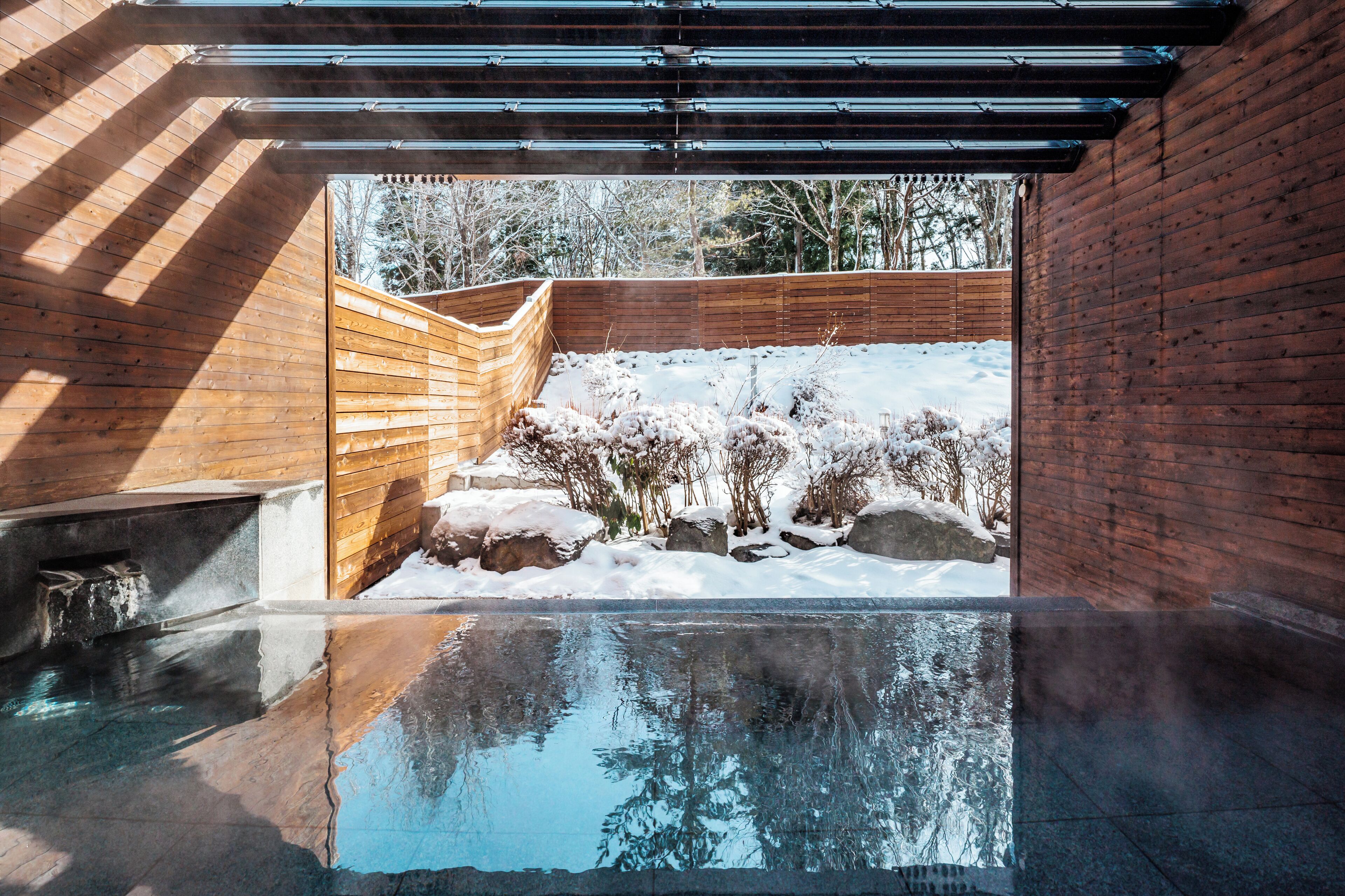 A spa area with a hot tub, wooden deck, and a view of a snowy landscape.