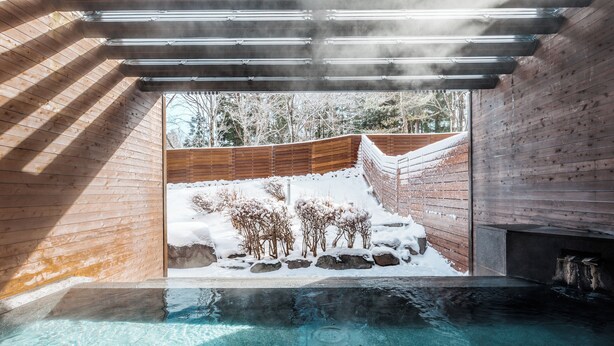 Un área de spa con interiores de madera, una piscina cristalina y vistas a un paisaje nevado al aire libre.