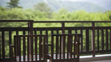 Relax on the balcony with a view of lush green surroundings and a serene mountain range.