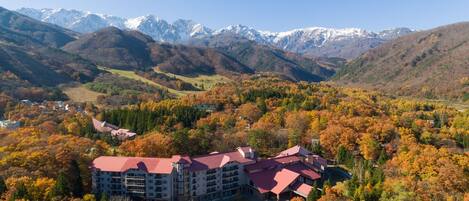 A hotel with a red roof, surrounded by autumn foliage and mountains in the background.