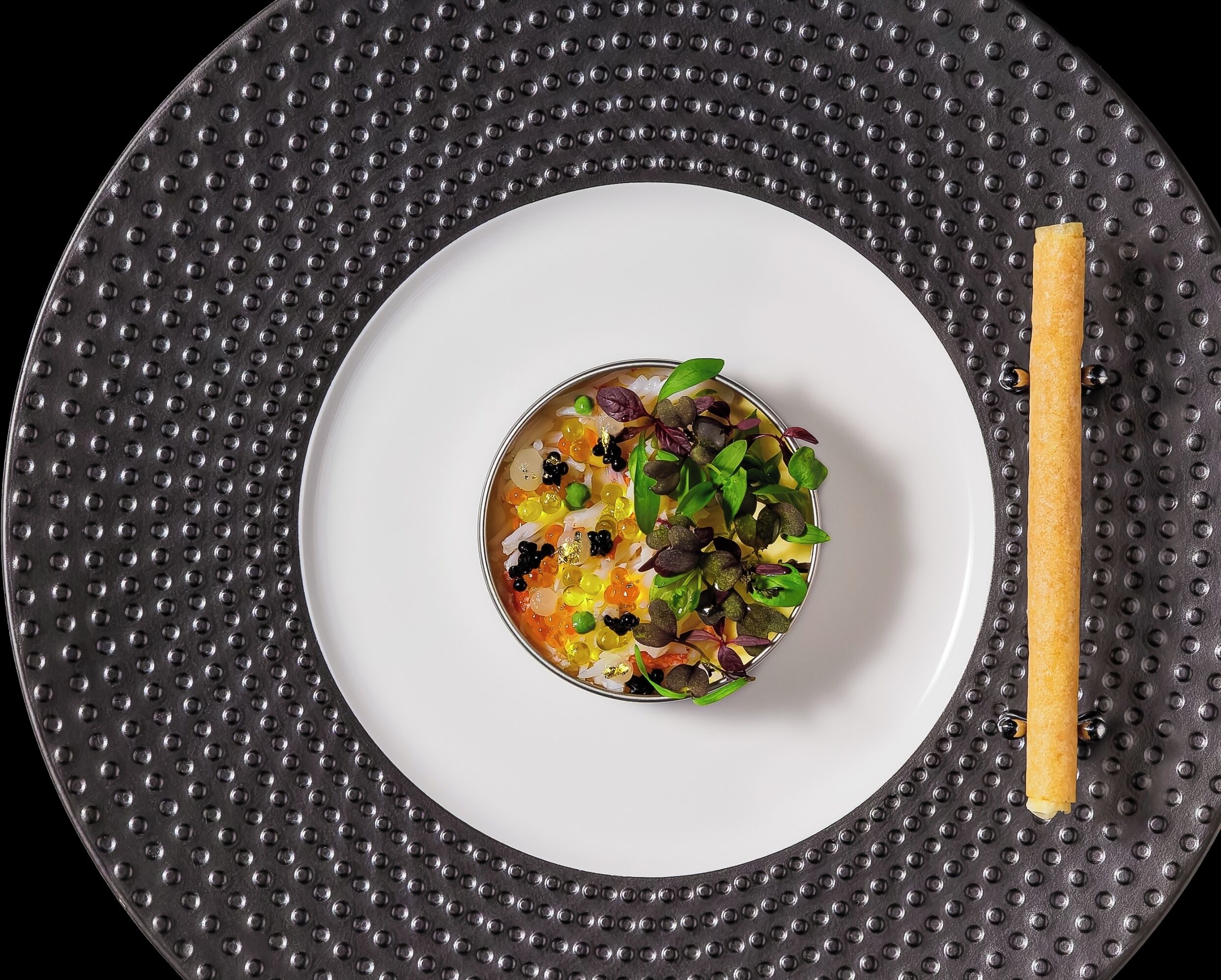 A white plate with a colorful salad and a piece of bread on a textured black mat.