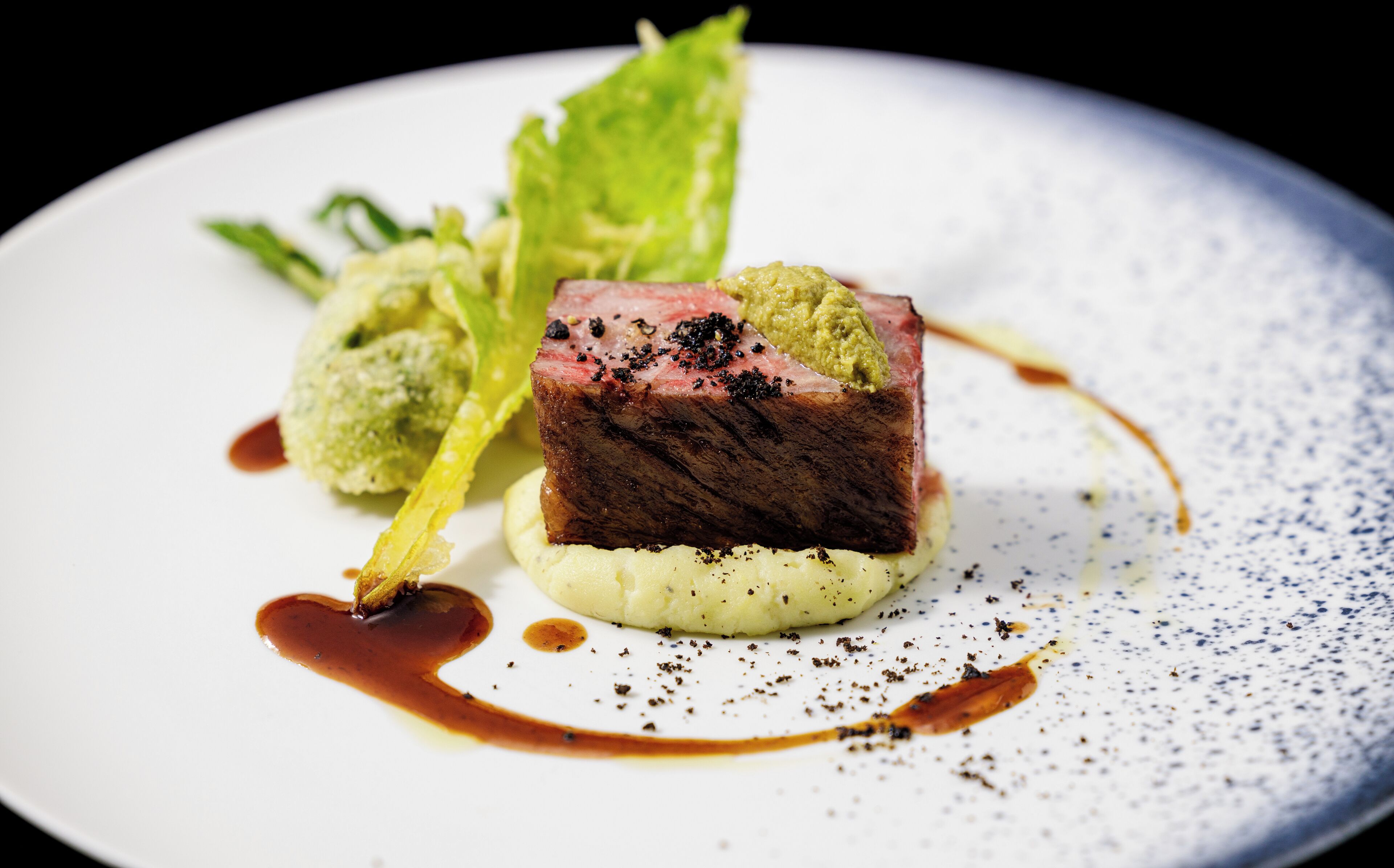 A plate with a piece of meat, green sauce, and a small mound of mashed potatoes.