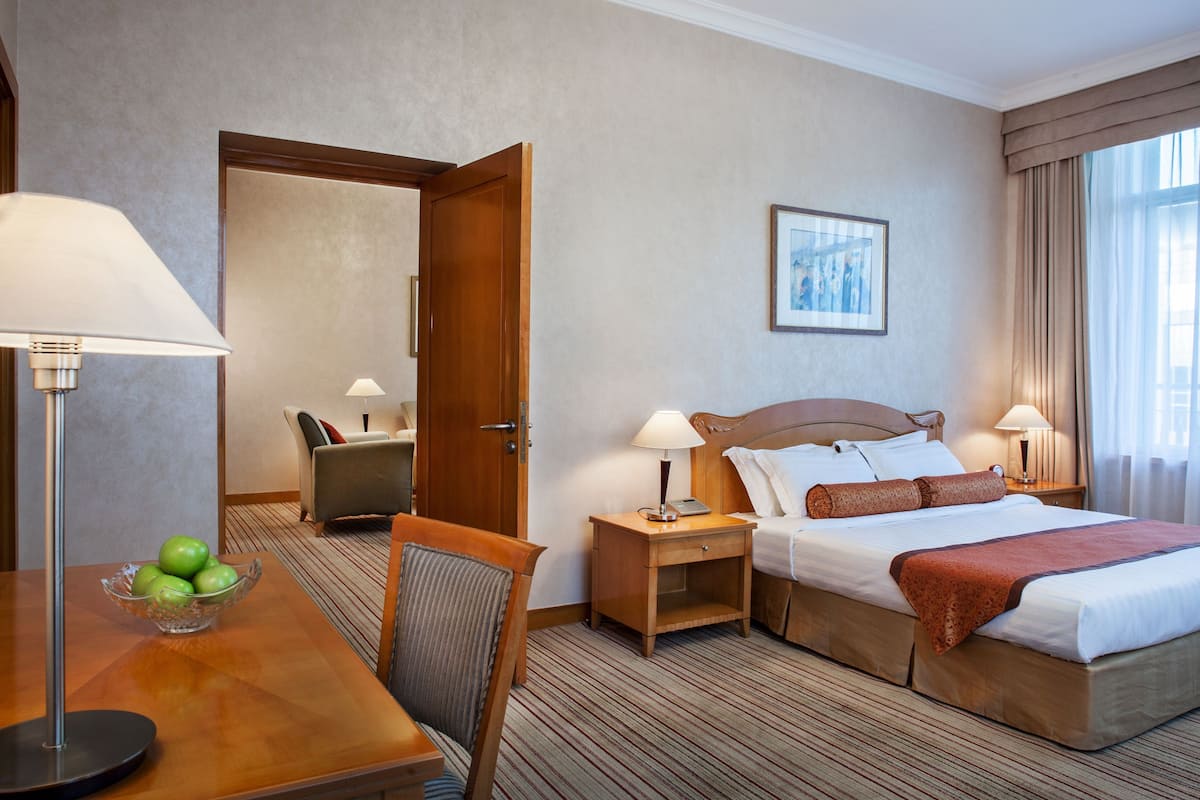 Ein Hotelzimmer mit einem Bett, Nachttischen, einem Sessel, einem Schreibtisch und einer Schüssel Äpfel.
