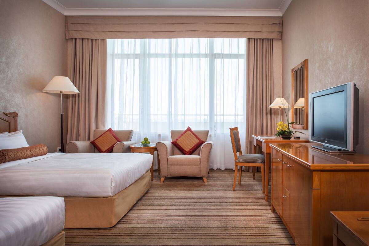 Ein Hotelzimmer mit einem großen Bett, einem Schreibtisch mit Fernseher, einem Sessel und einem kleinen Tisch mit Lampe.