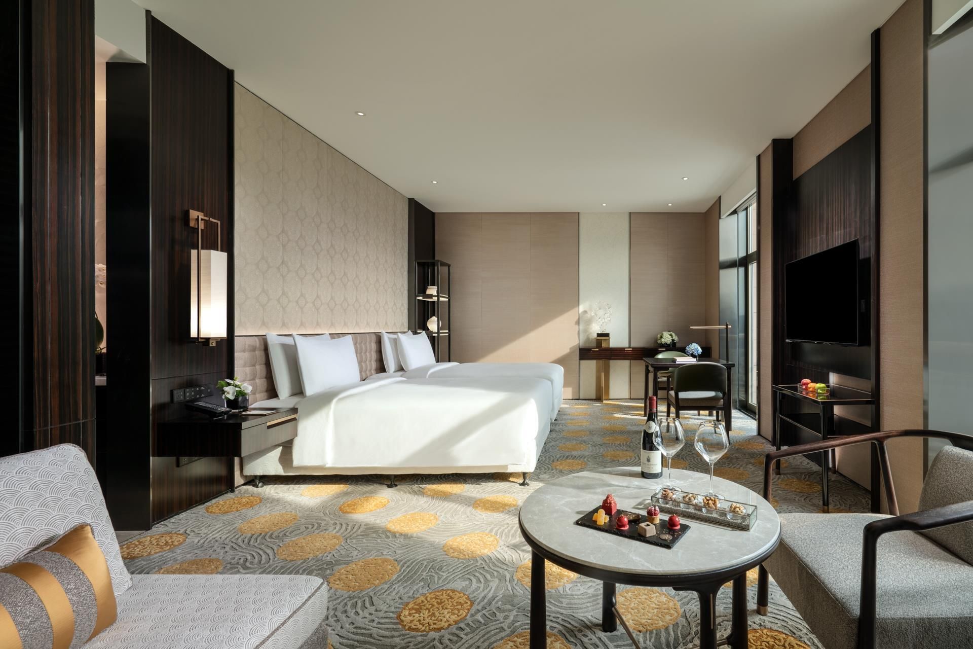 Habitación de hotel con una cama grande, un escritorio con silla, televisión y una mesa redonda con aperitivos.