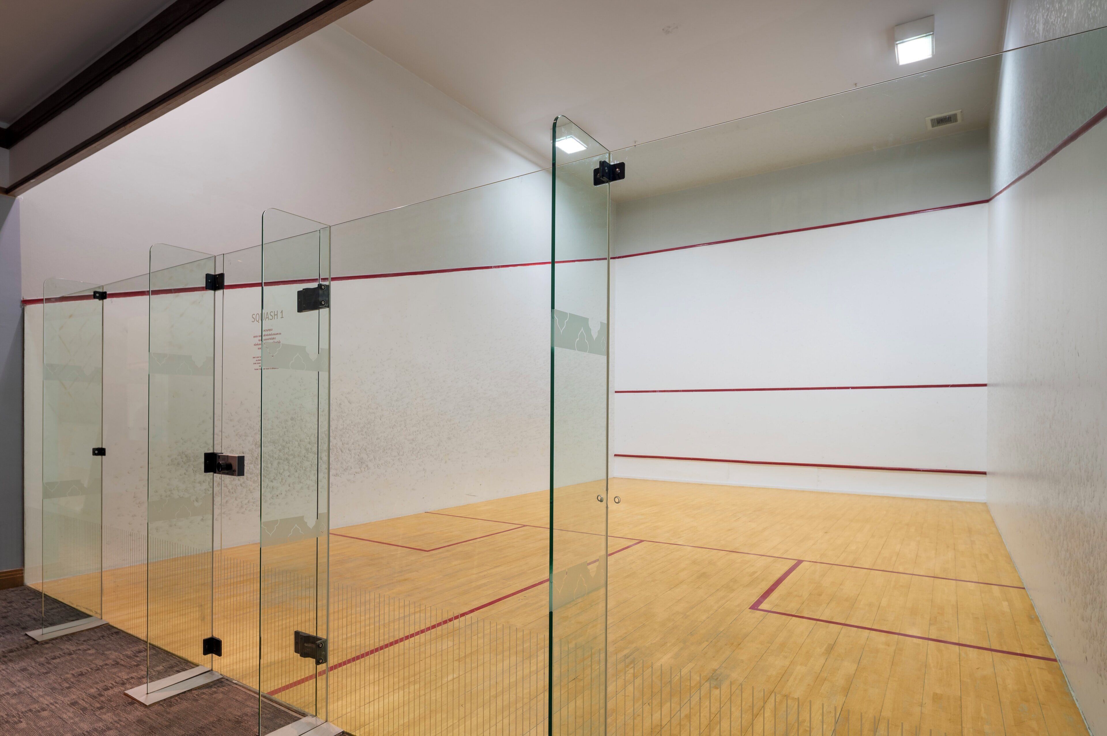 A squash court with glass walls and a wooden floor.