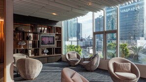 A modern living room with a large TV, comfortable seating, a bookshelf, and a city view through large windows. - Amari Bangkok (Bangkok)