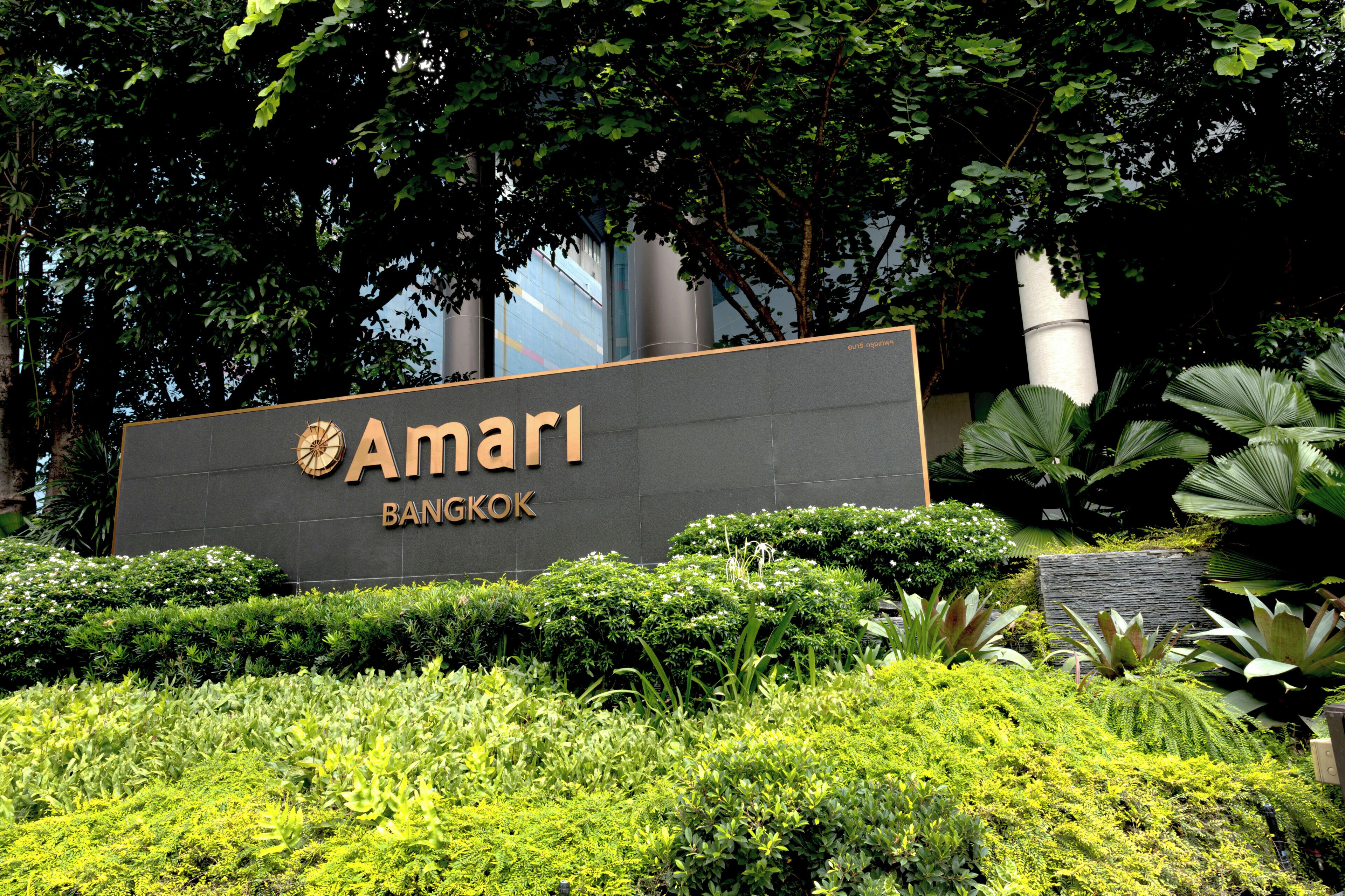 Ein Schild für das Amari Bangkok mit modernem Design, umgeben von üppiger Vegetation und einem gepflegten Garten.