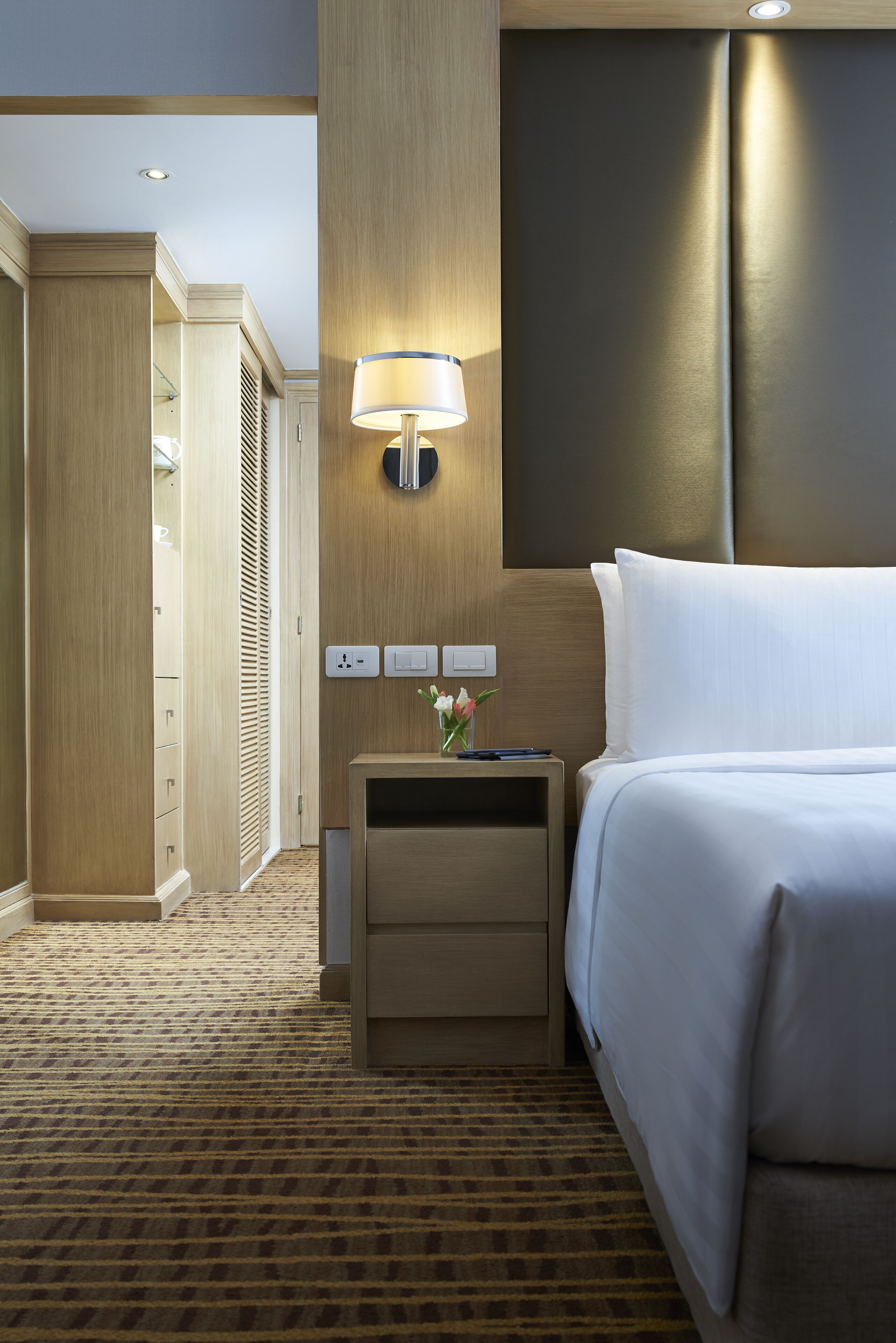A hotel room with a bed, bedside table, lamp, and a wardrobe.