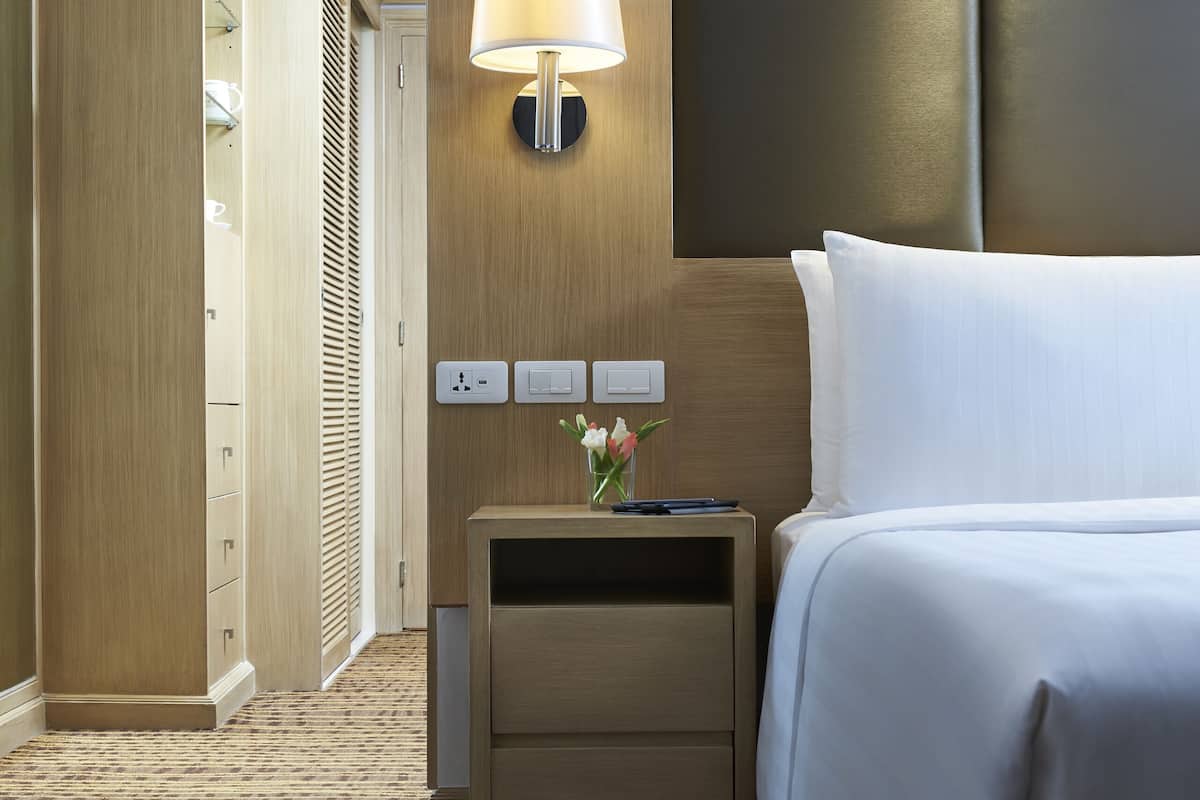 A hotel room with a bed, bedside table, lamp, and a wardrobe.