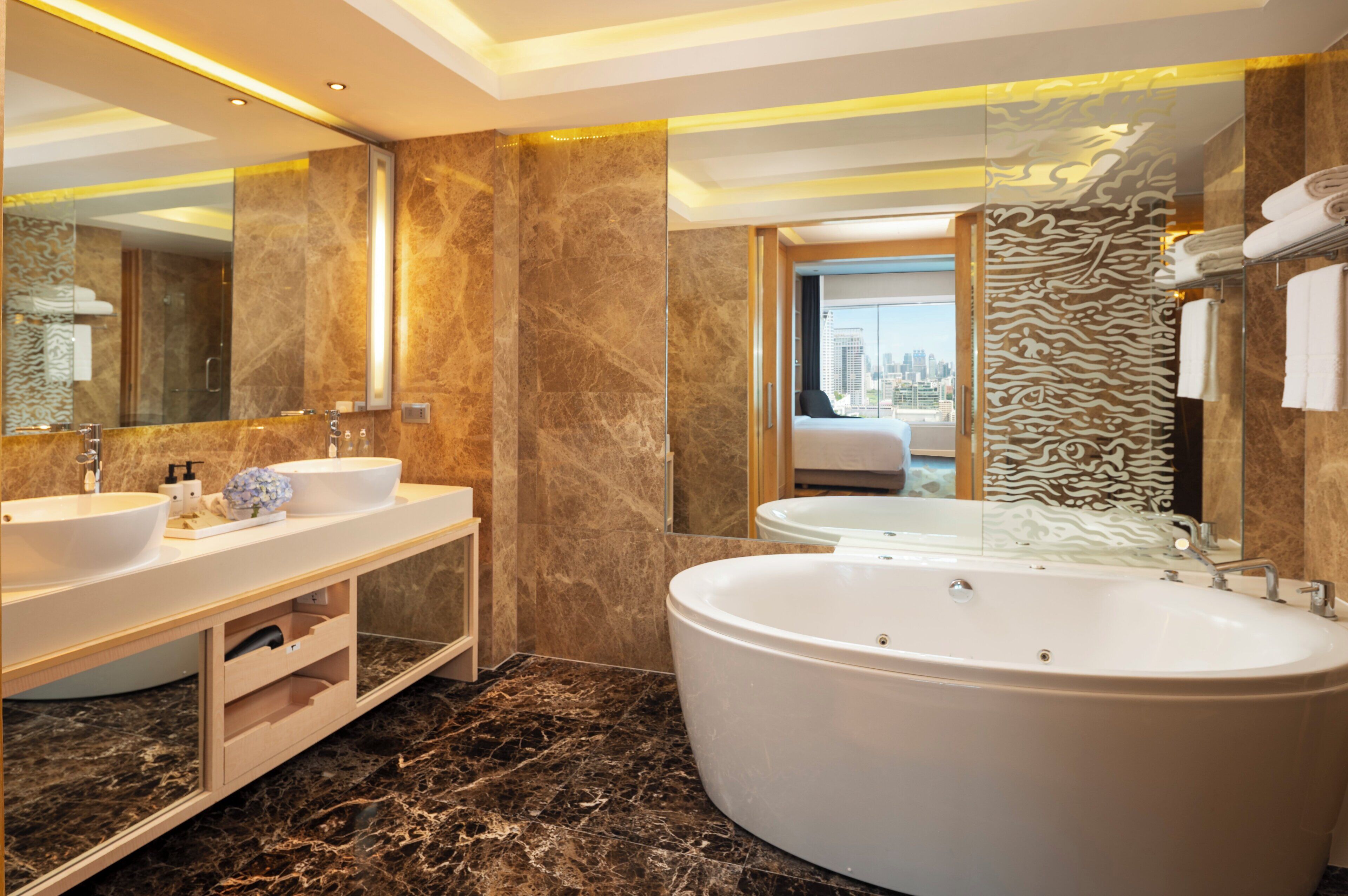 A modern bathroom with two sinks, a large bathtub, and a city view through the glass door.