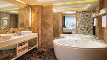 A modern bathroom with two sinks, a large bathtub, and a city view through the glass door.