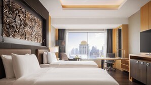A hotel room with two beds, a desk, a chair, a TV, and a large window with a city view. - Amari Bangkok (Bangkok)
