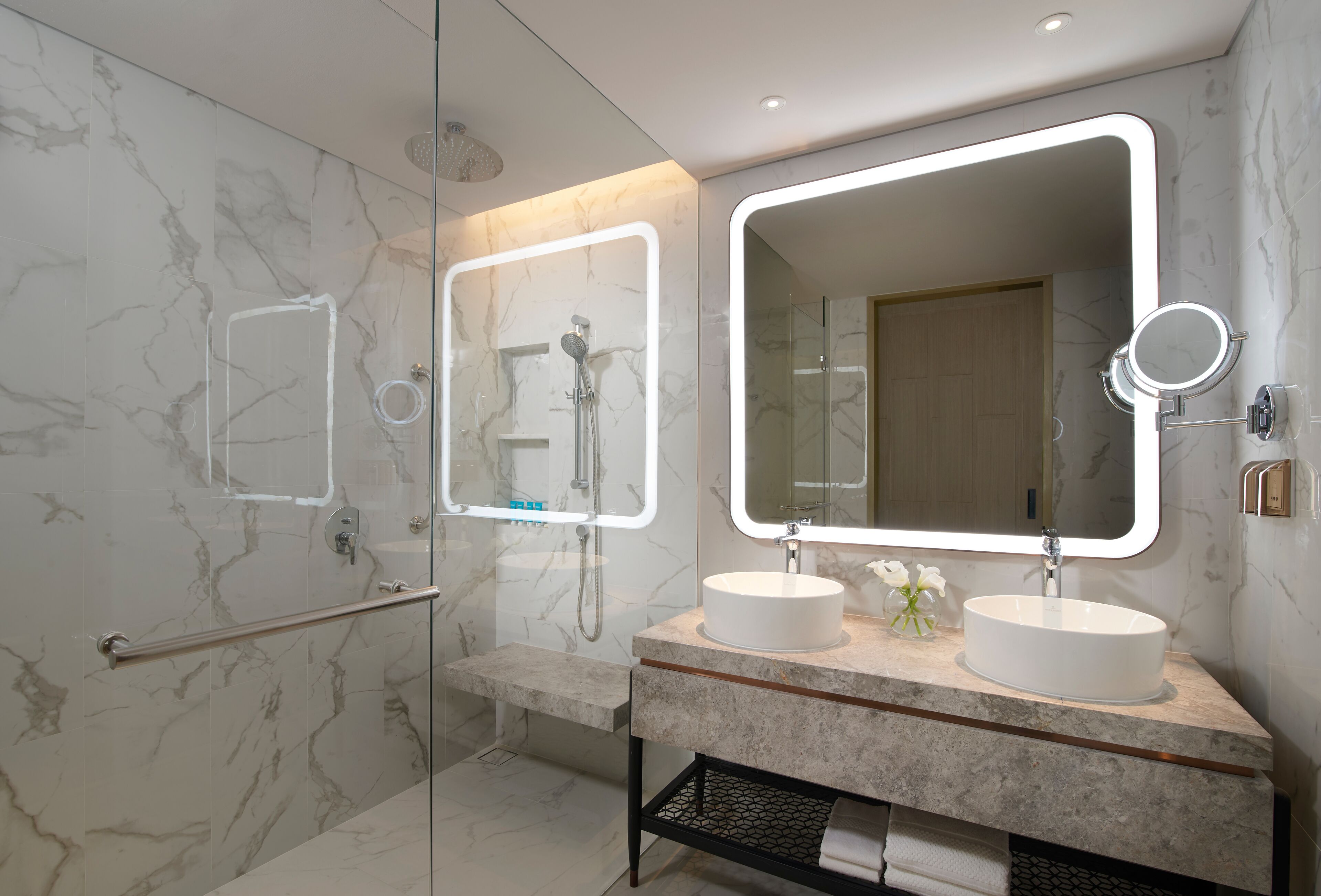 A modern bathroom with two sinks, a large mirror, and a shower area.