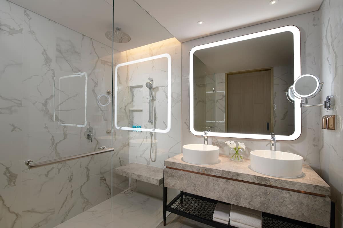 A modern bathroom with two sinks, a large mirror, and a shower area.