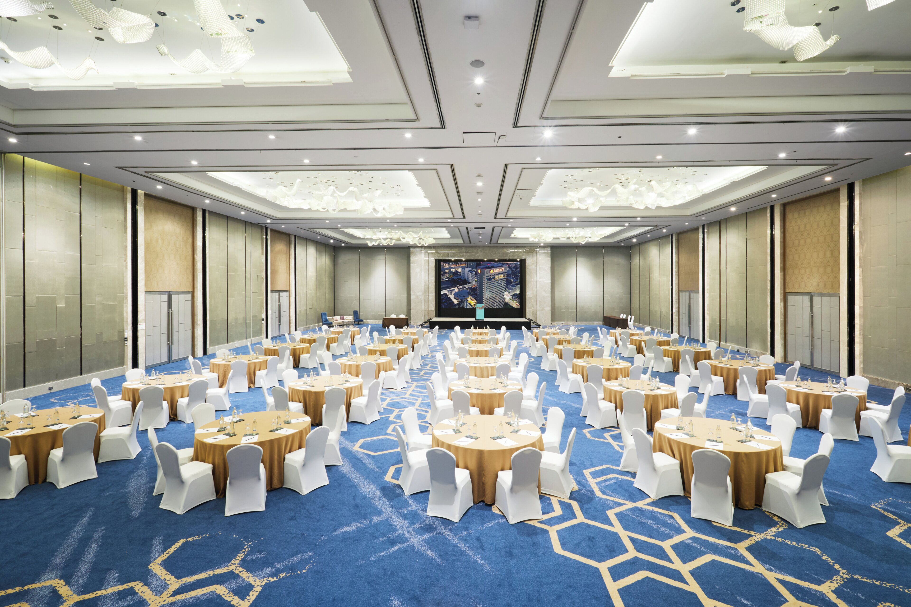 Un salón de conferencias amplio con mesas redondas, sillas blancas y alfombra azul.