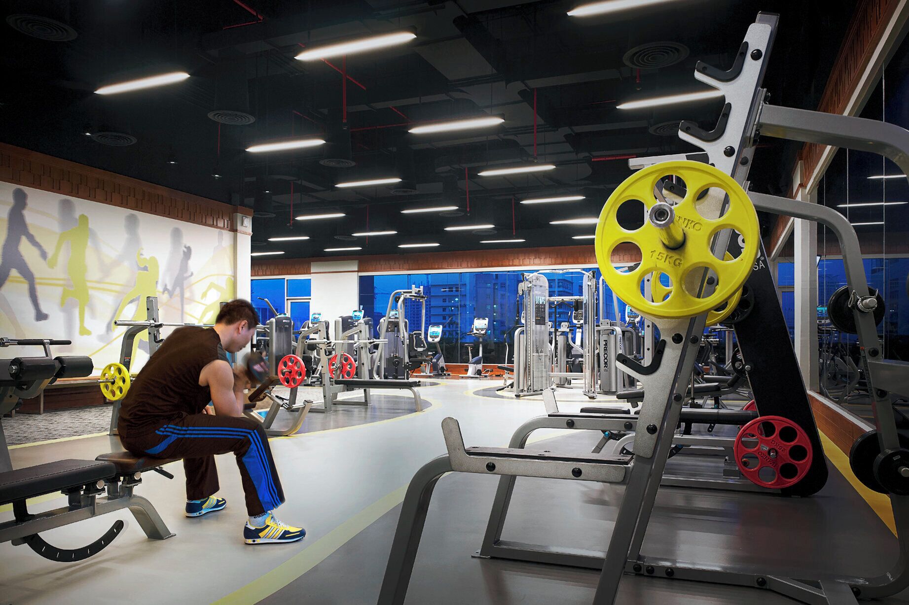 A gym with various exercise equipment, a bench, and a person using a machine.