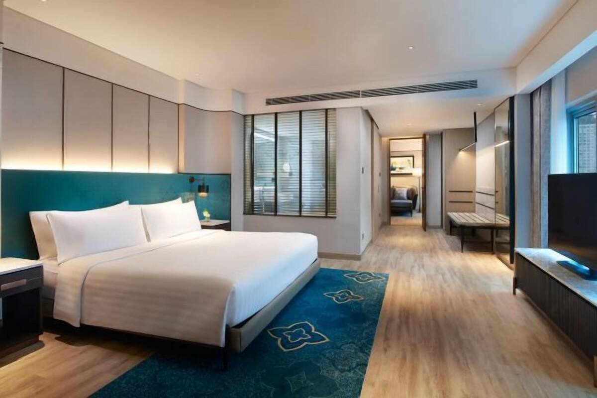 Une chambre d’hôtel moderne dotée d’un grand lit, d’un bureau, d’une télévision et d’une salle de bain visible à travers une porte en verre.
