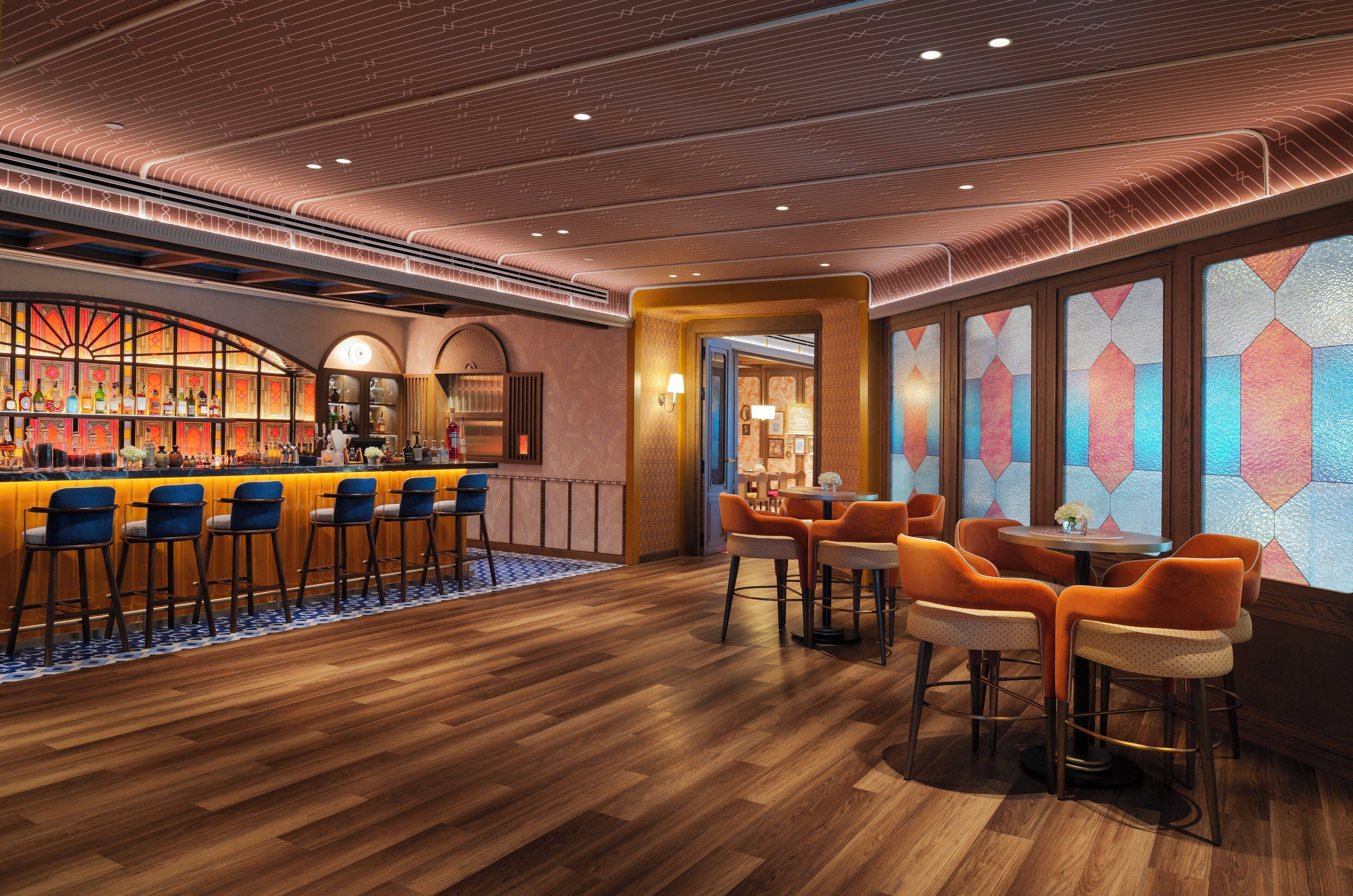 A bar area with wooden flooring and bar stools, a seating area with round tables and chairs, and a decorative wall with geometric patterns.