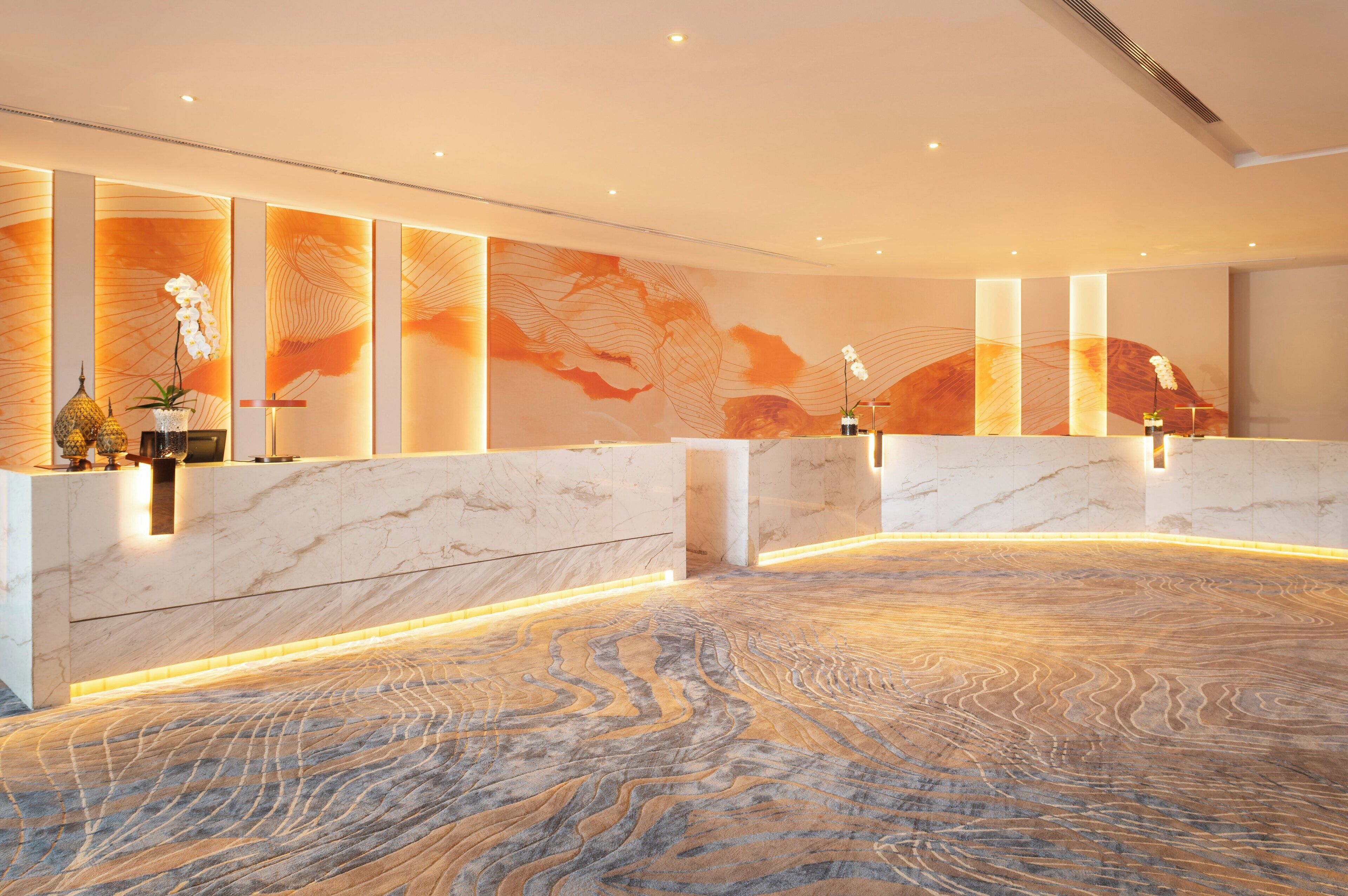 A spacious lobby with marble reception counters, a patterned floor, and a large wall mural.