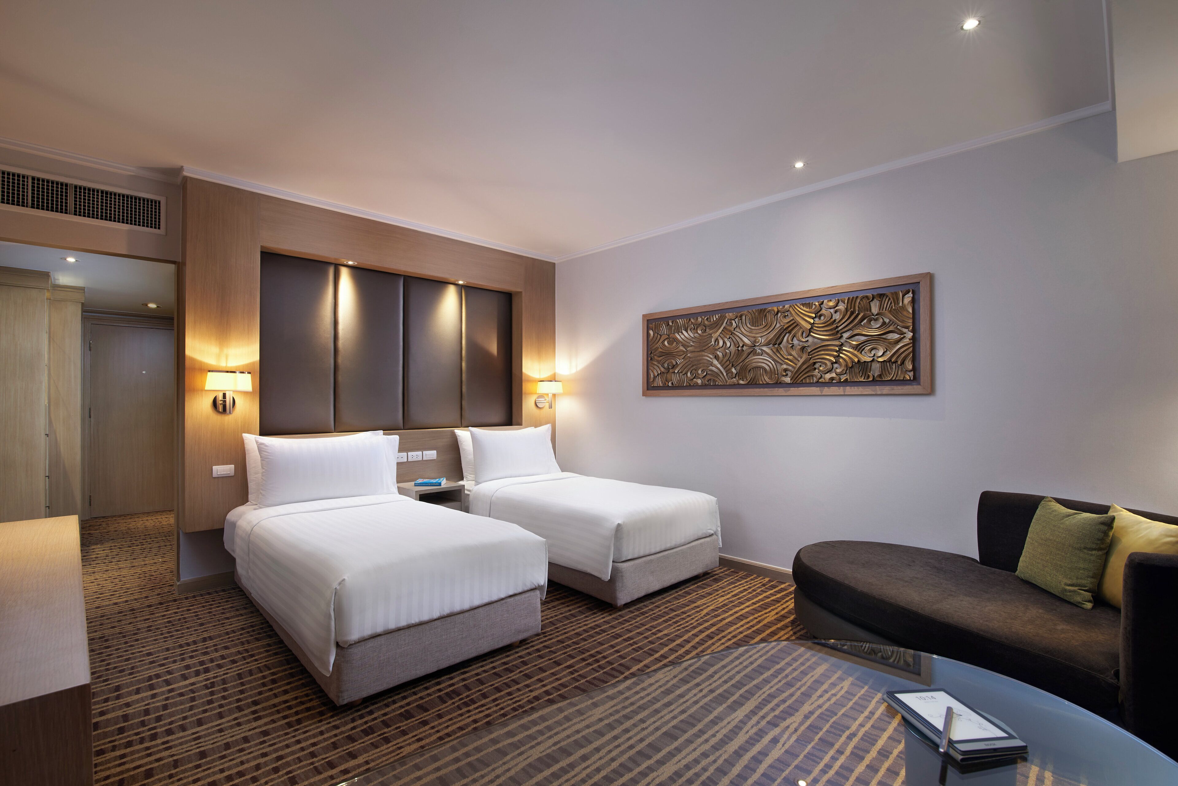 A hotel room with two beds, a sofa, a coffee table, and a decorative wall piece.