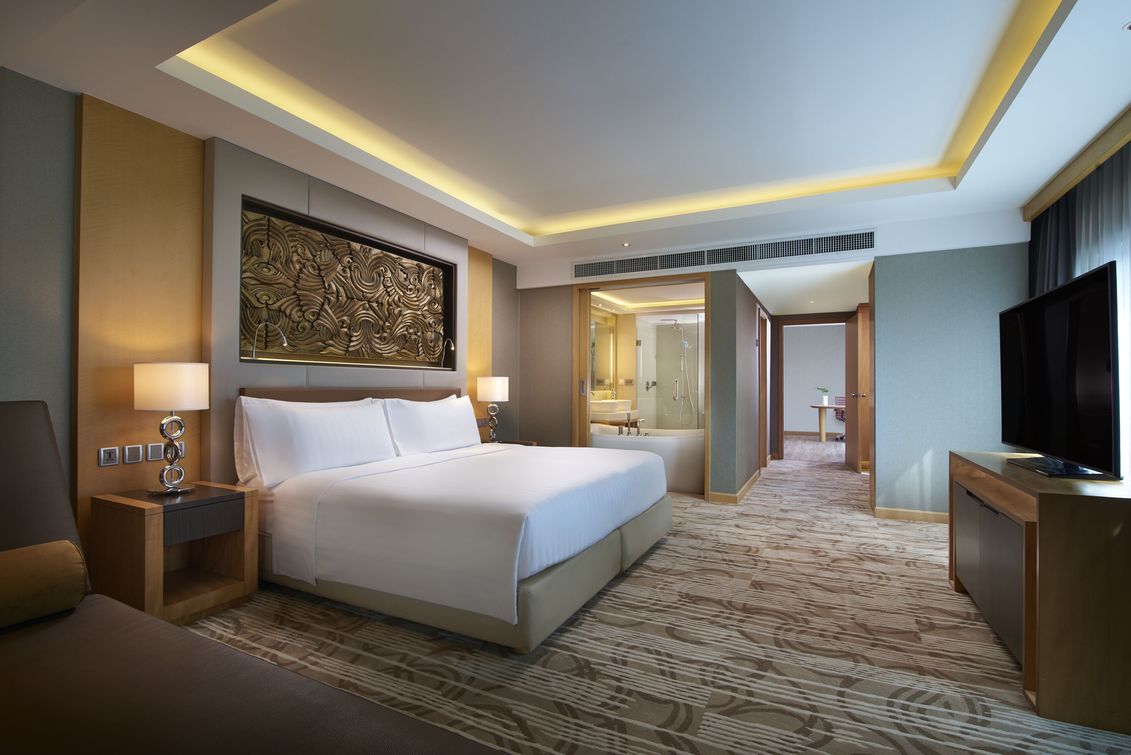 A hotel room with a large bed, a TV, a desk, and a bathroom visible through an open door.