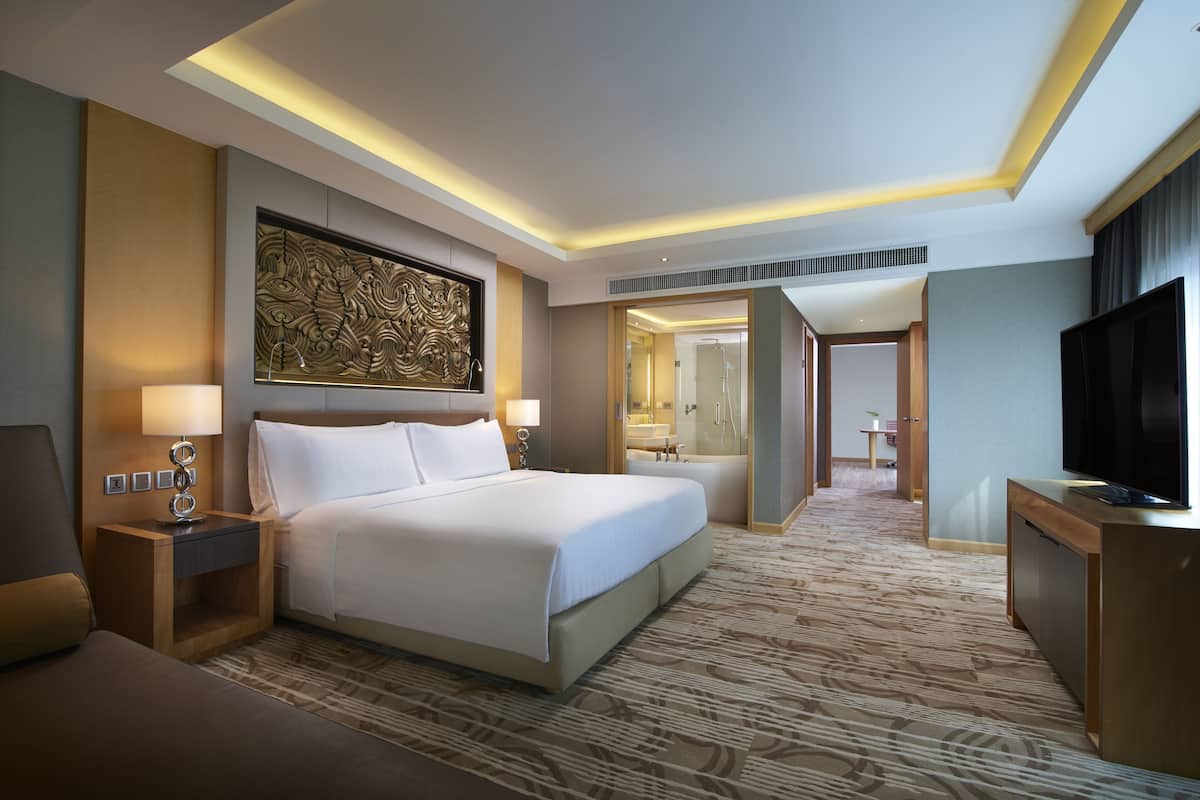 A hotel room with a large bed, a TV, a desk, and a bathroom visible through an open door.