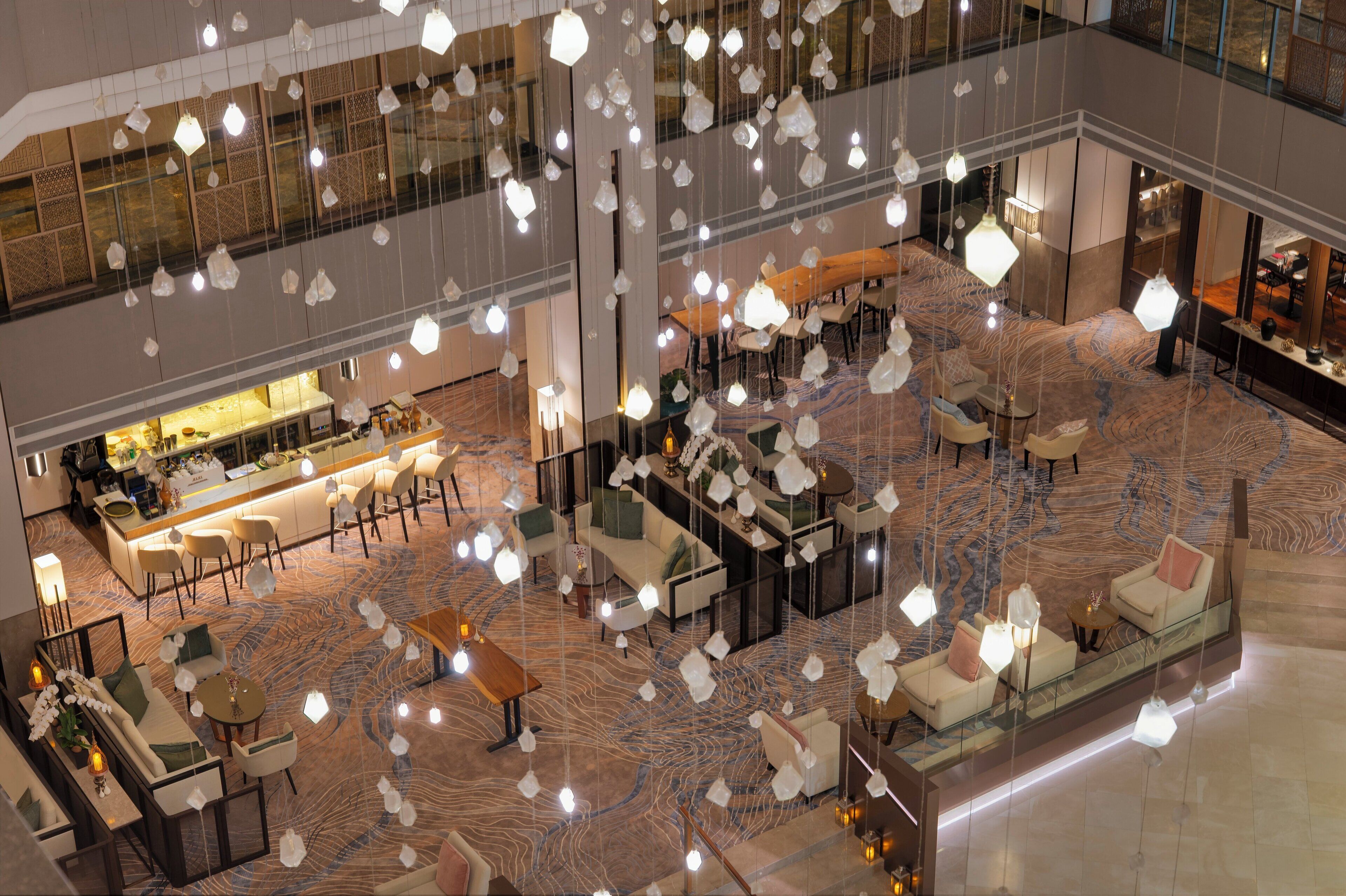 A spacious lobby with multiple seating areas, a bar, and hanging light fixtures.