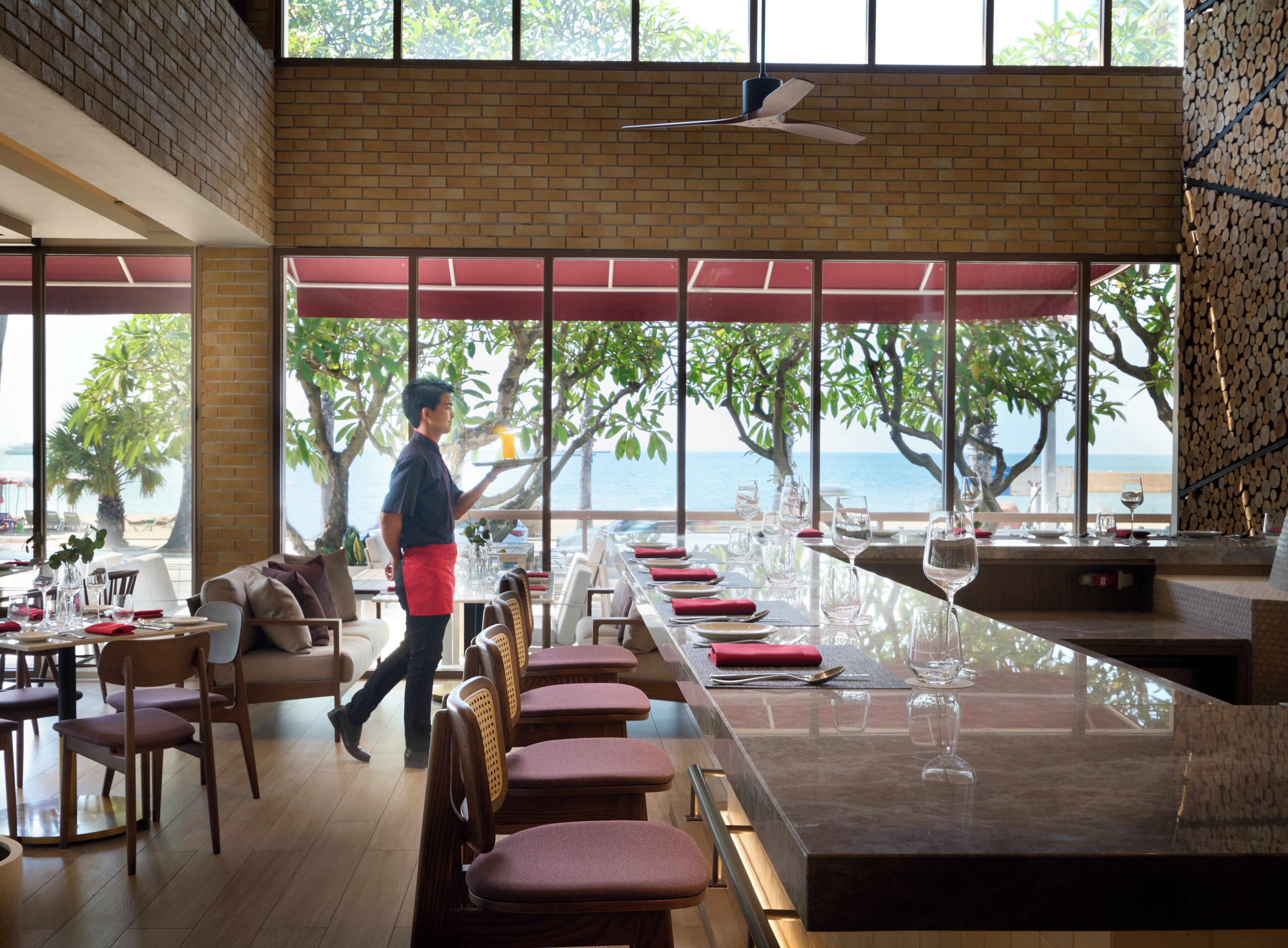 Un restaurante con una barra larga, varias mesas y vistas al mar.