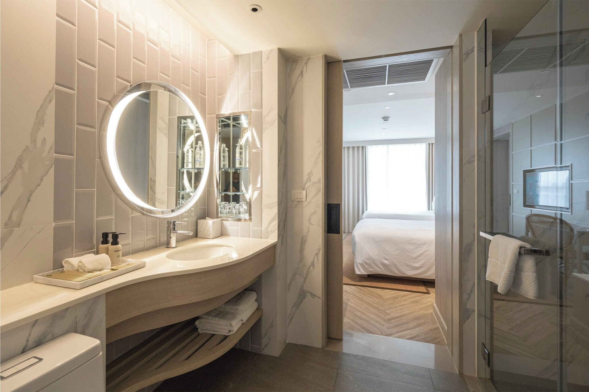 A modern bathroom with a marble vanity, a round mirror, and a glass shower enclosure.