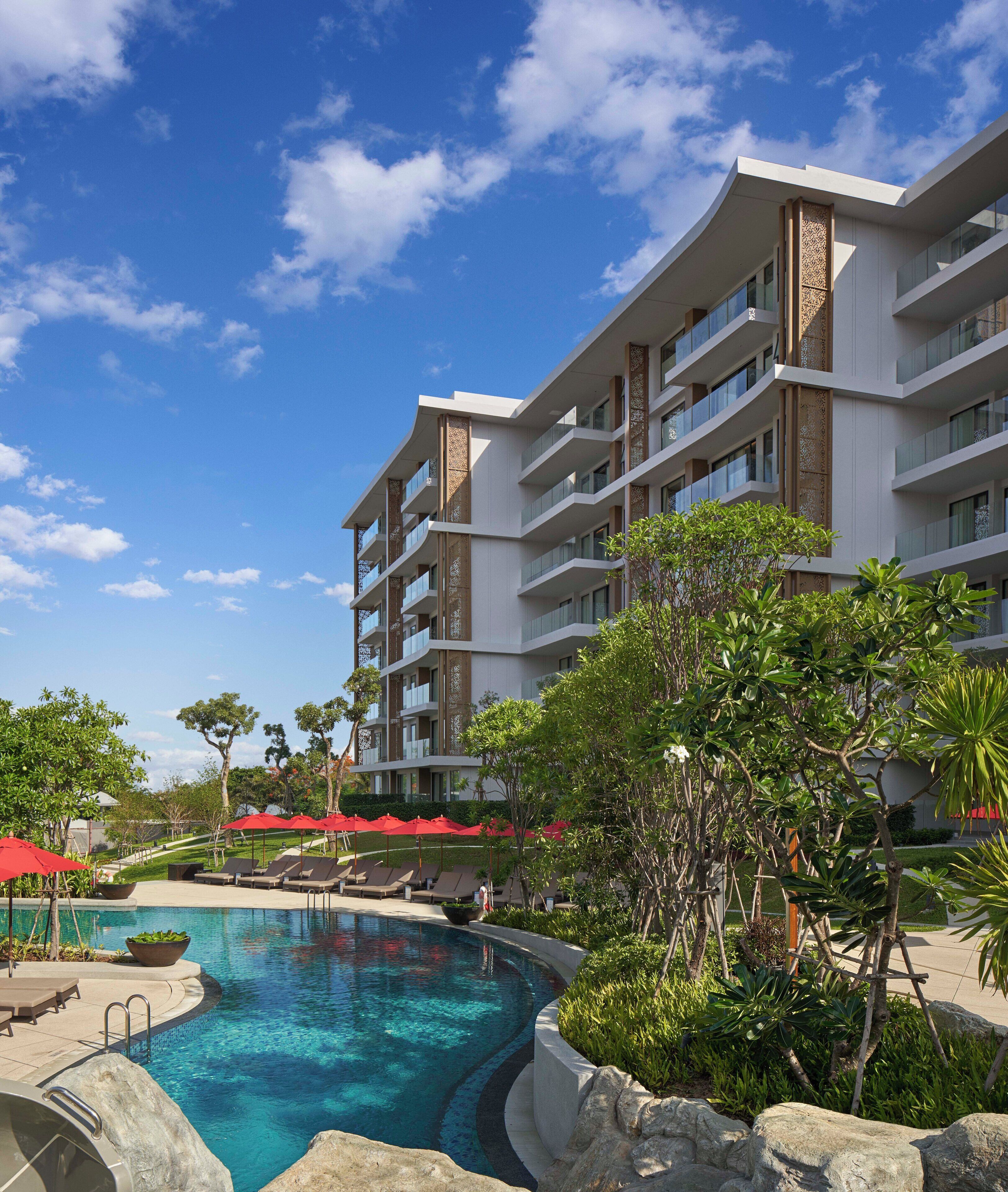 A hotel with a swimming pool, multiple balconies, and lush greenery.