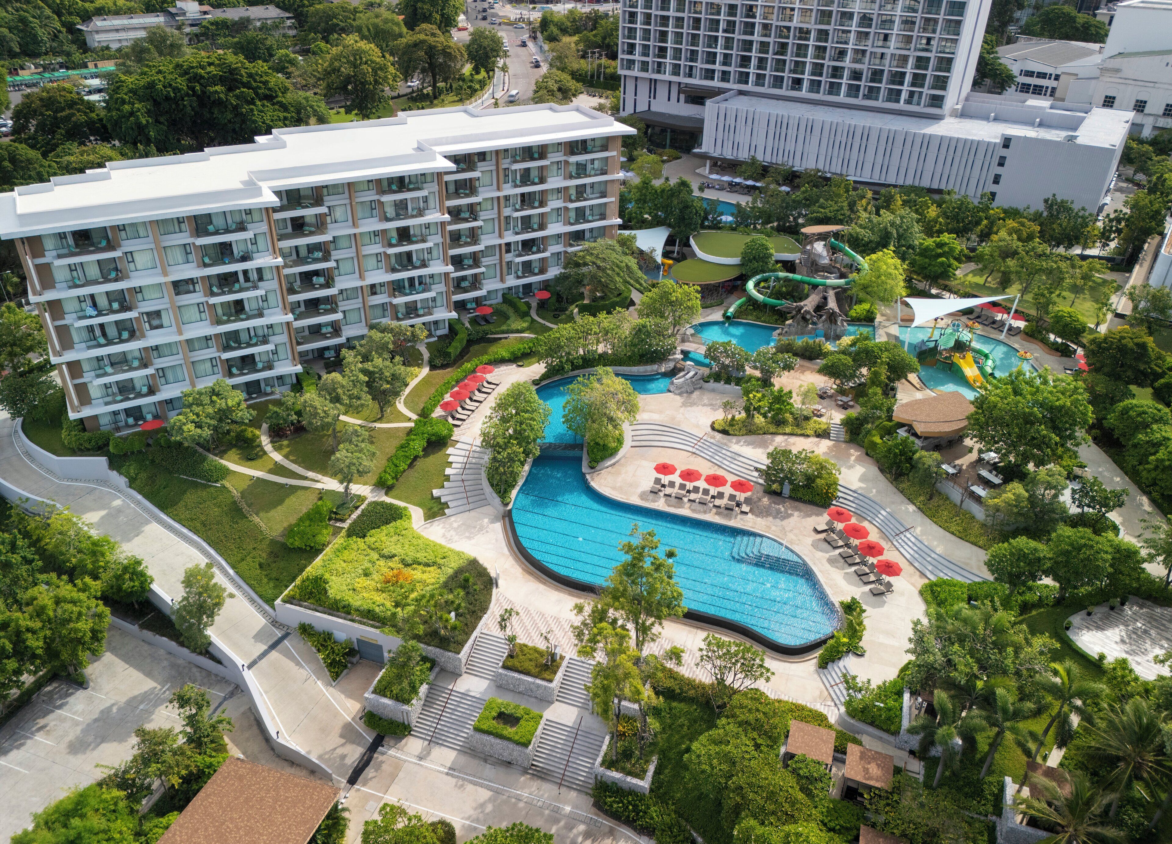 A hotel with a large swimming pool, multiple balconies, and lush landscaping.