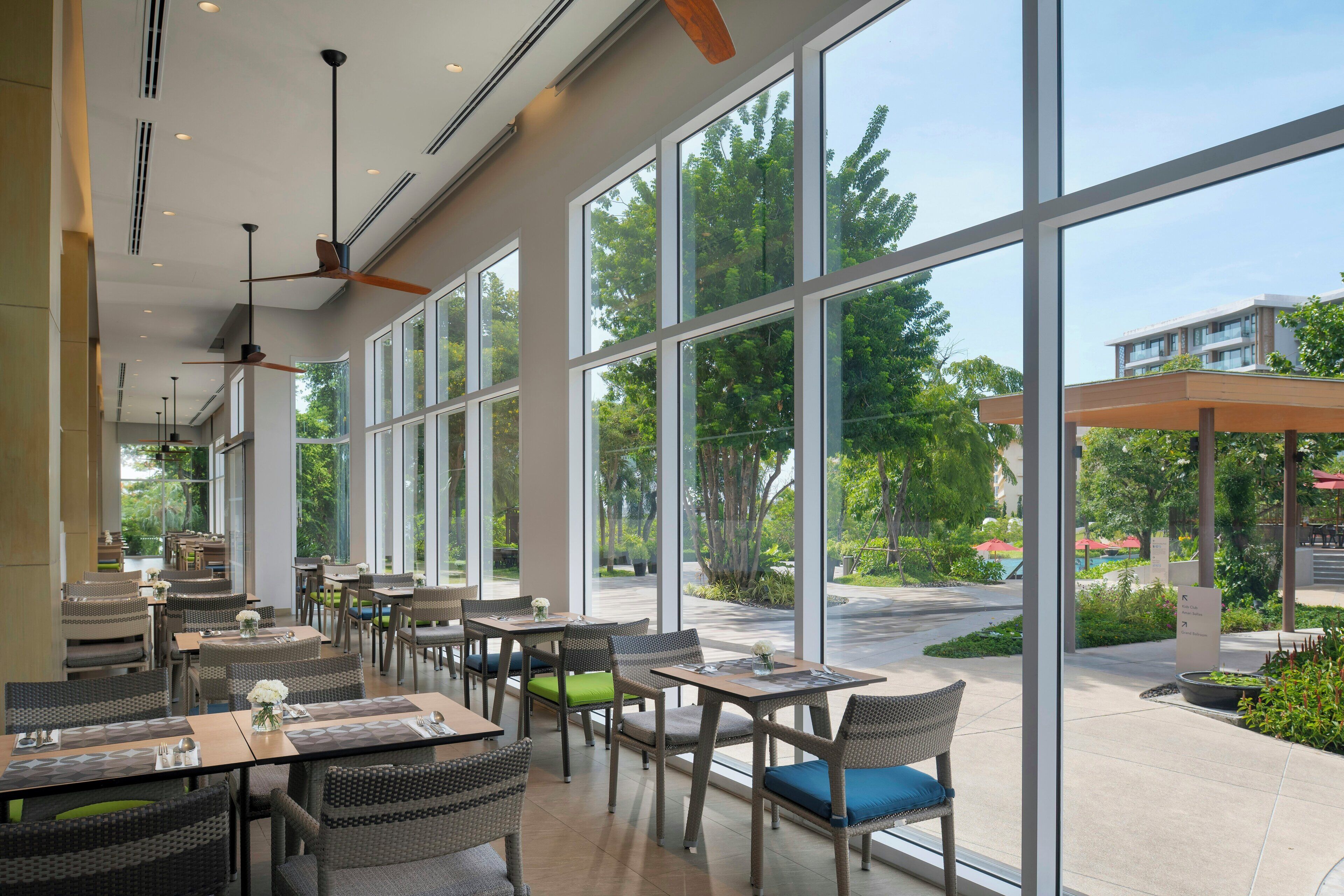 A spacious indoor dining area with large windows, wicker furniture, and ceiling fans.