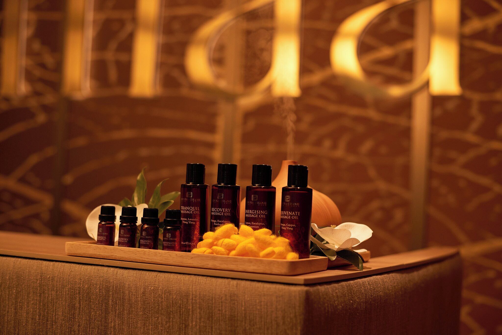 A wooden tray with several bottles of massage oil and a bowl of yellow beads.