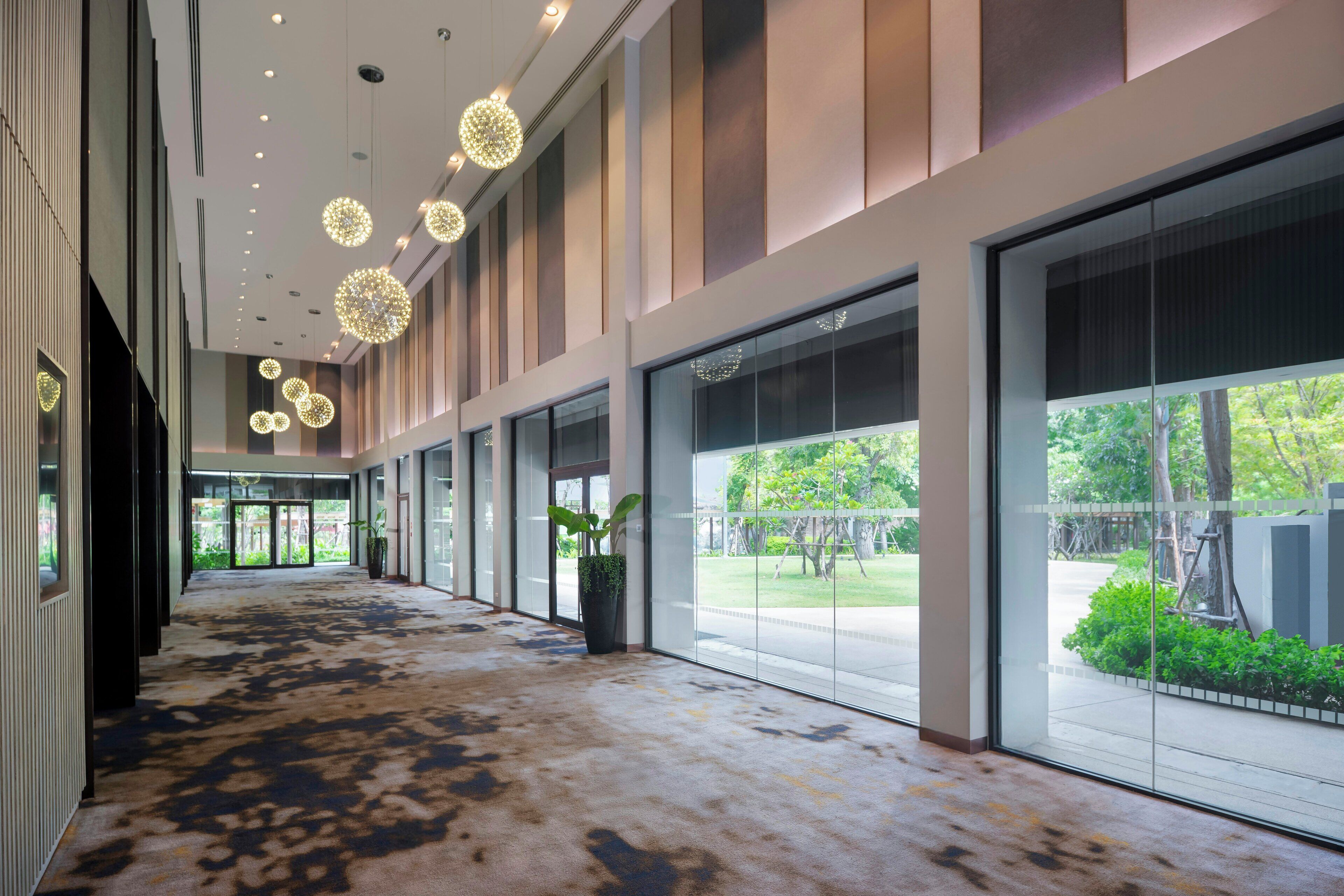 A spacious corridor with large windows, a patterned carpet, and decorative spherical lights.