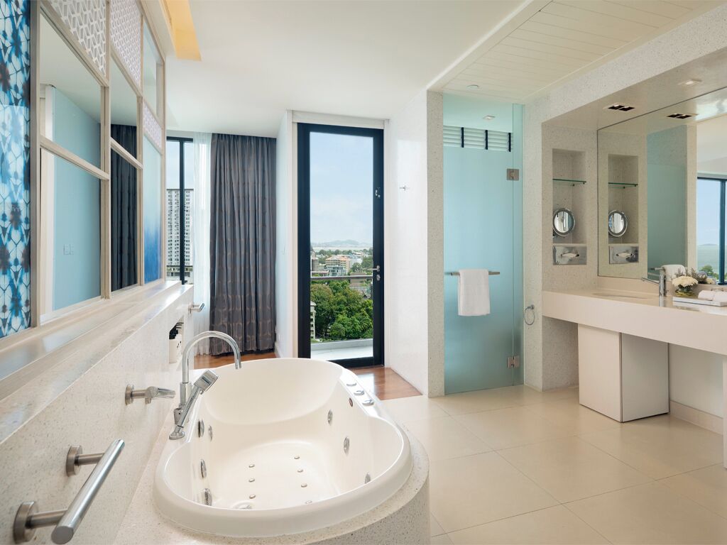 Un baño moderno con una bañera grande, cabina de ducha independiente, tocador con espejo y vistas a la ciudad a través de una puerta de cristal.