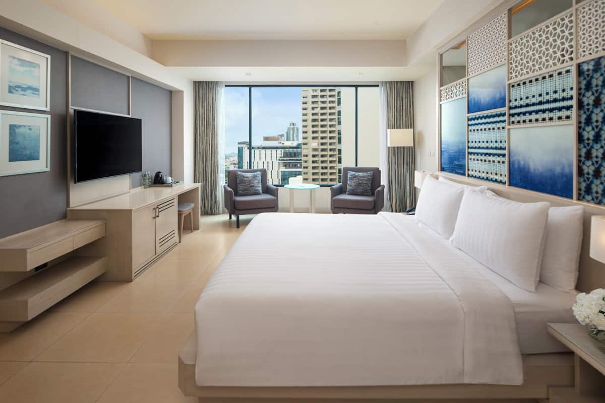 A hotel room with a large bed, a TV, a desk, and a view of the city.
