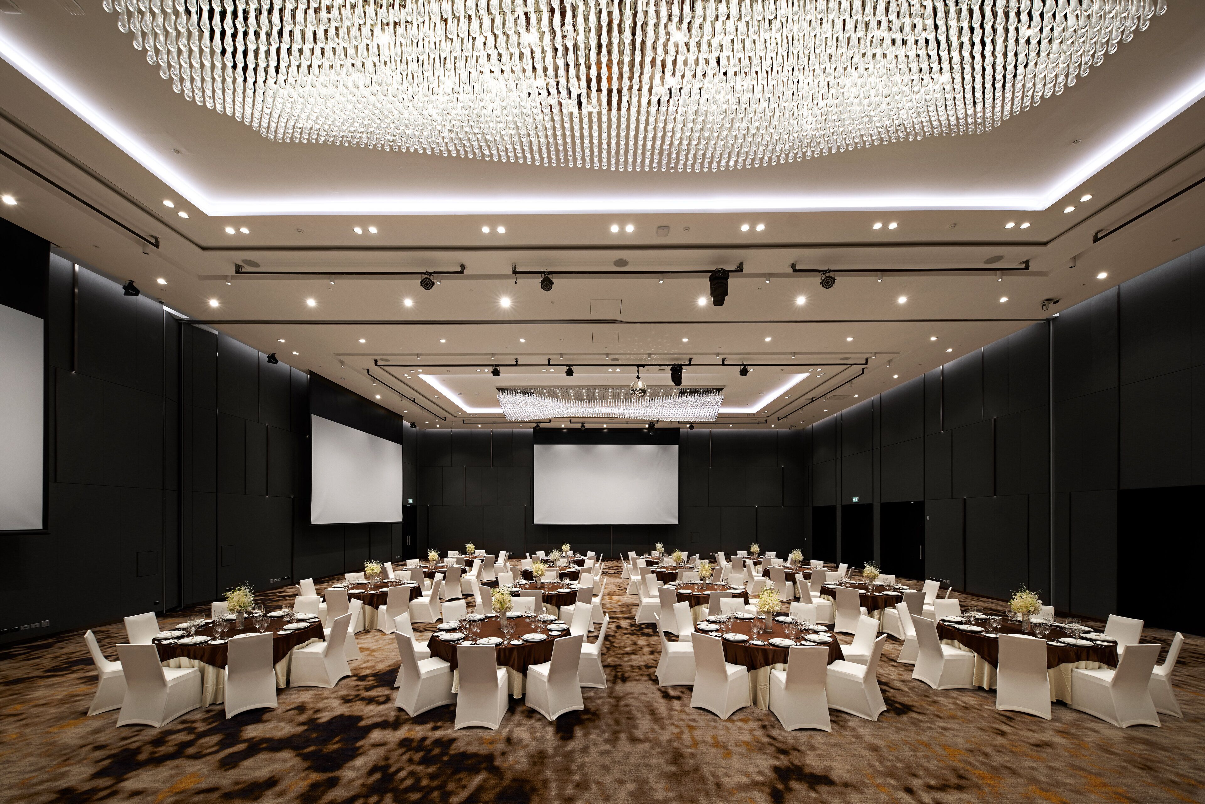 A large conference room with rows of tables and chairs, a large screen, and a modern chandelier.