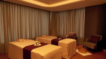 A spa room with two massage tables, a chair, and a small table with bottles.