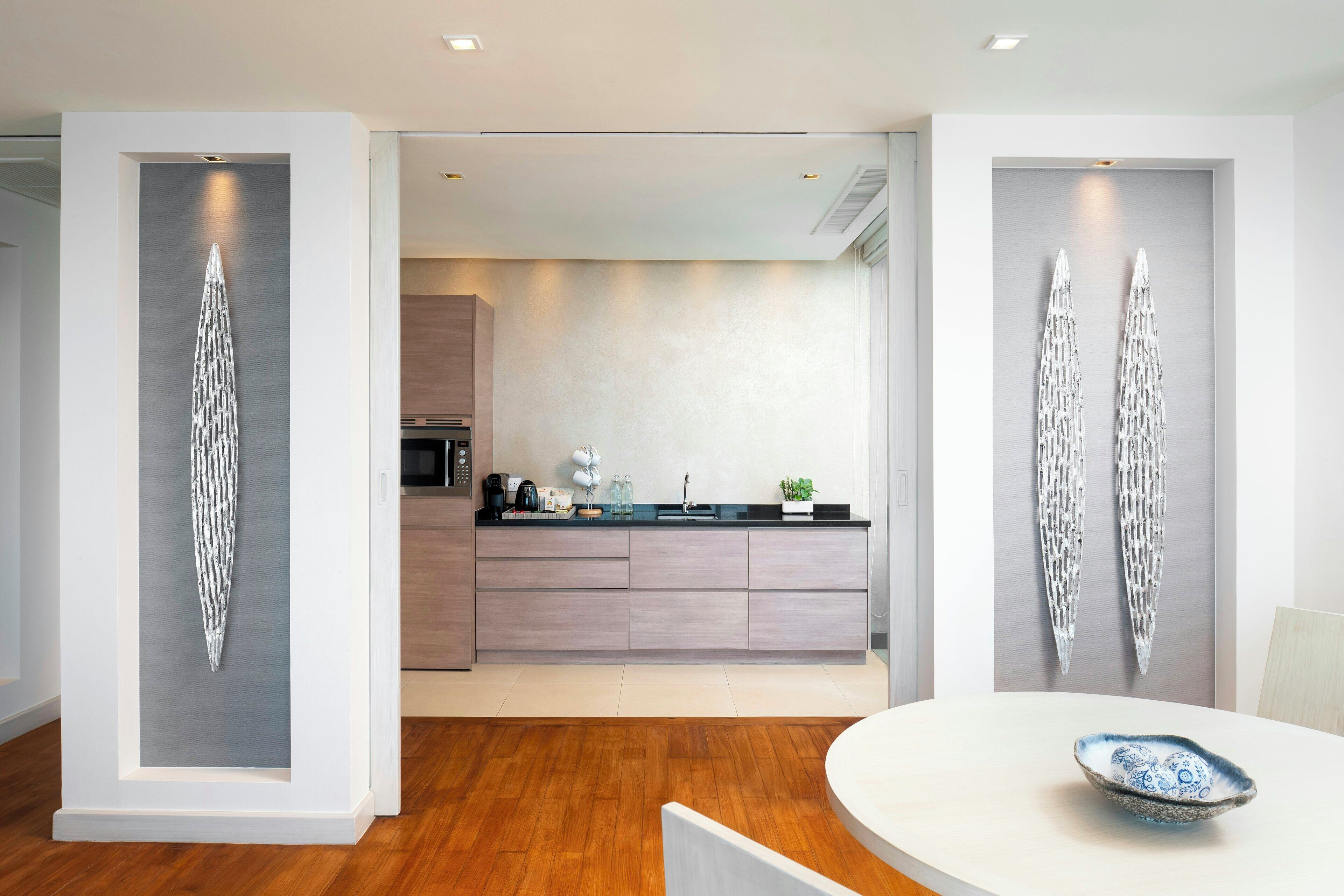 A modern kitchen with a central island, wooden flooring, and a dining area with a white table and blue bowl.