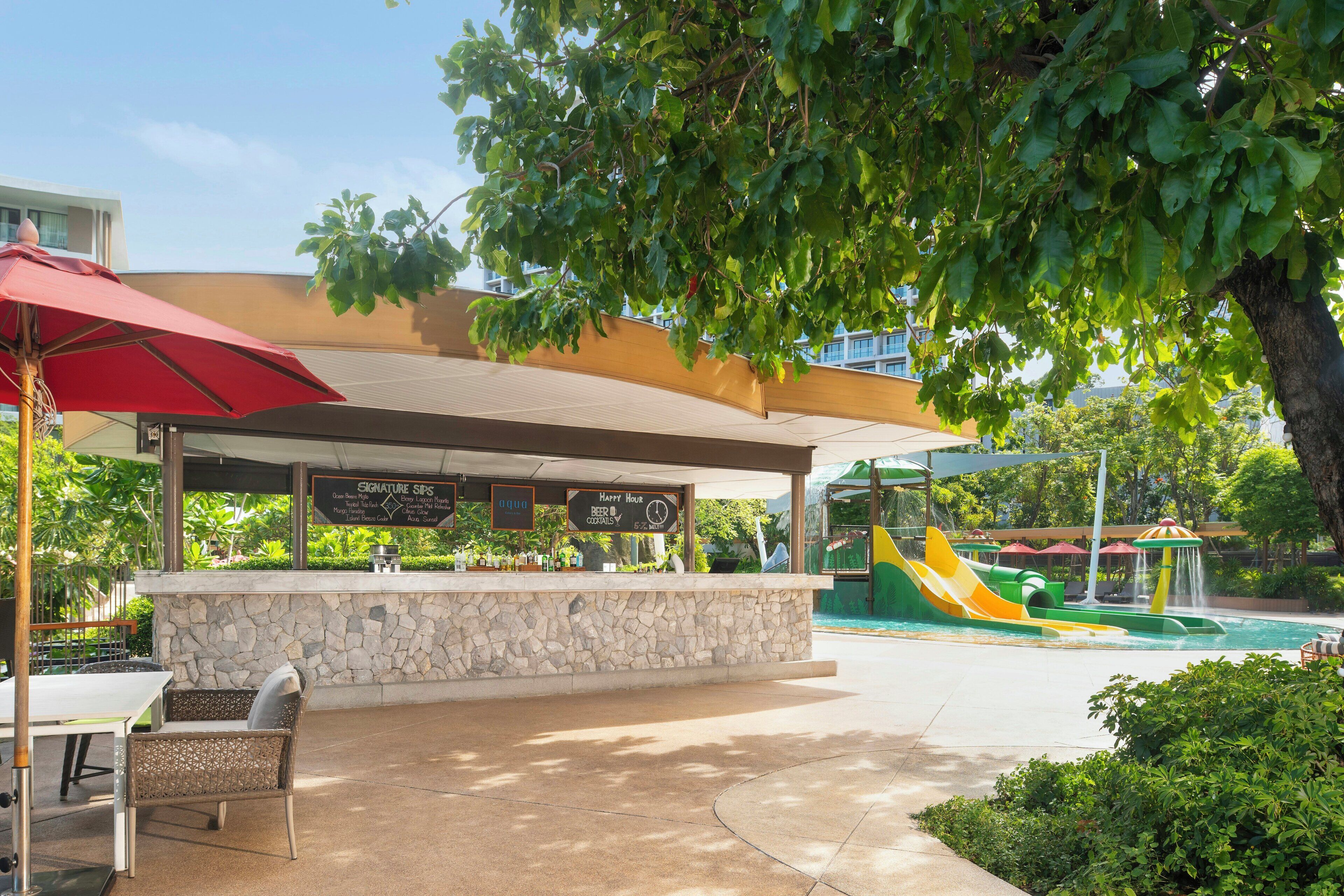 An outdoor bar area with a stone wall, seating, and a menu board.