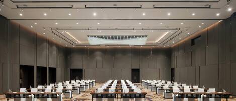 A large conference room with rows of tables and chairs, a chandelier, and recessed lighting.