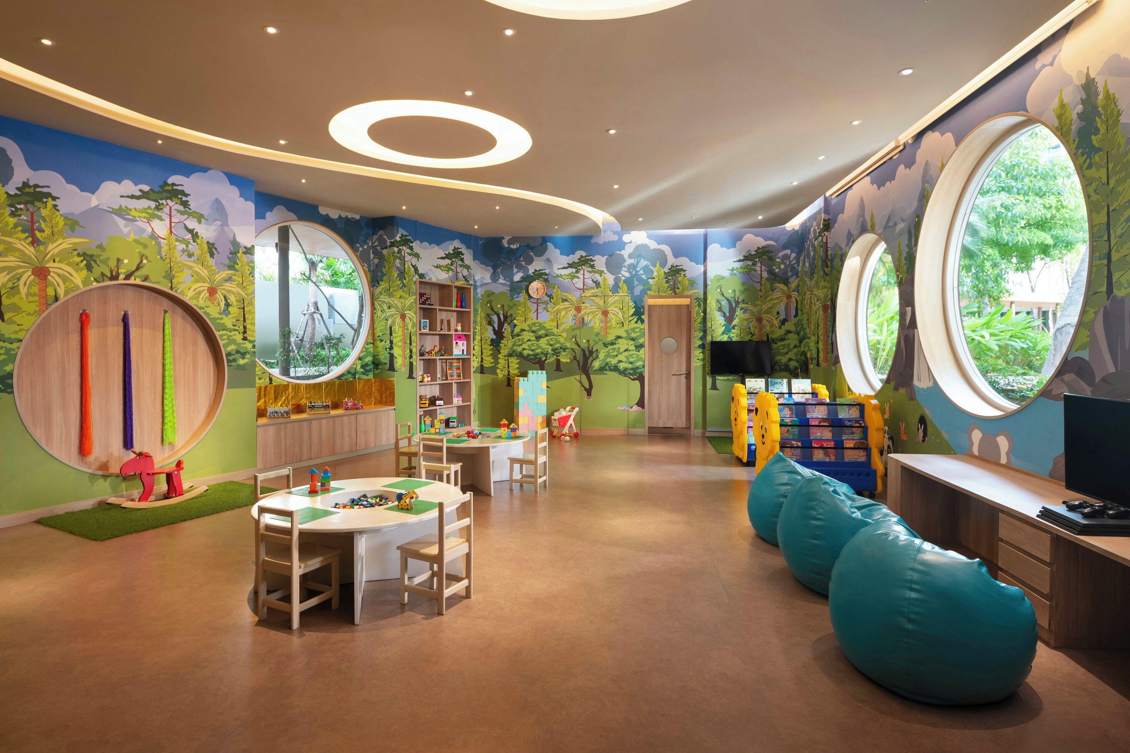 Un cuarto de juegos para niños con temática de selva, que incluye una mesa de juegos, pufs y una estantería.