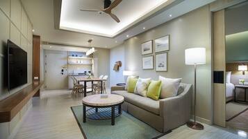 Un salon moderne avec un canapé, une table basse et un ventilateur de plafond. On y trouve également un coin repas avec des chaises et une table, ainsi qu’une cuisine en arrière-plan.