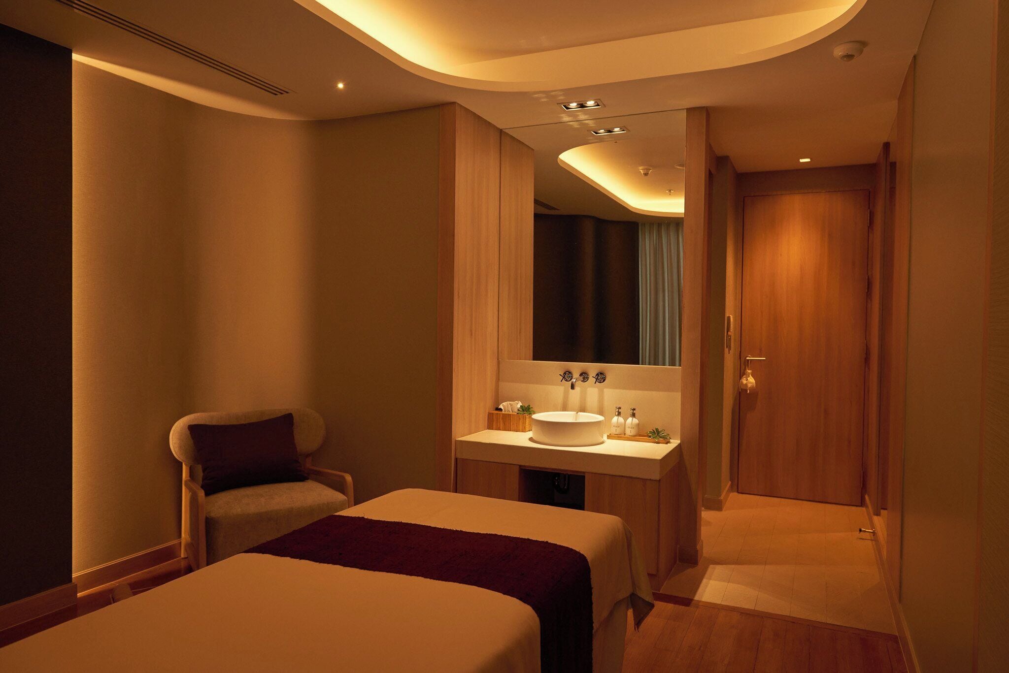 Een hotelkamer met een bed, een stoel, een badkamer met een wastafel en een spiegel.