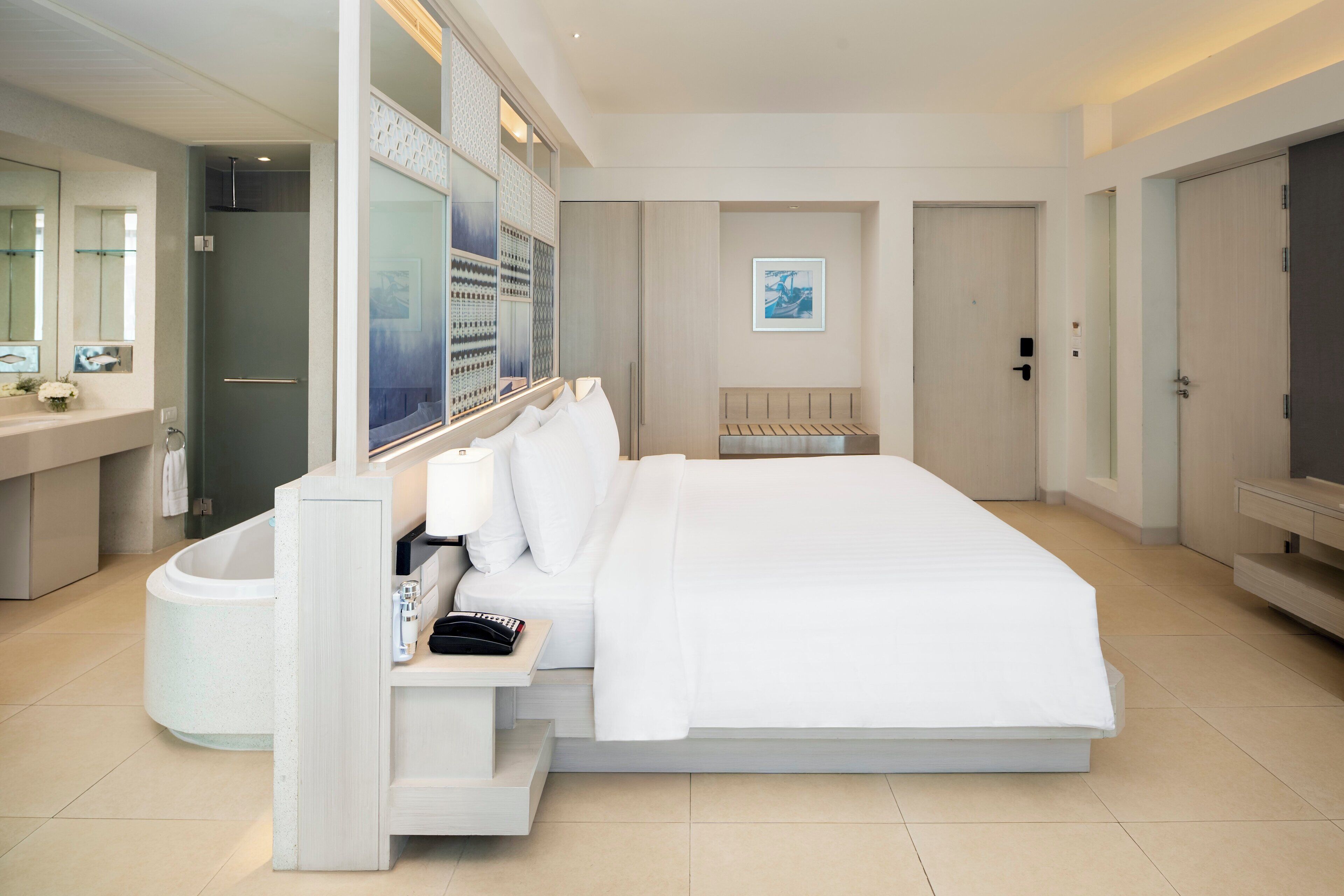 A modern hotel room with a large bed, a built-in vanity, a shower, and a small seating area.