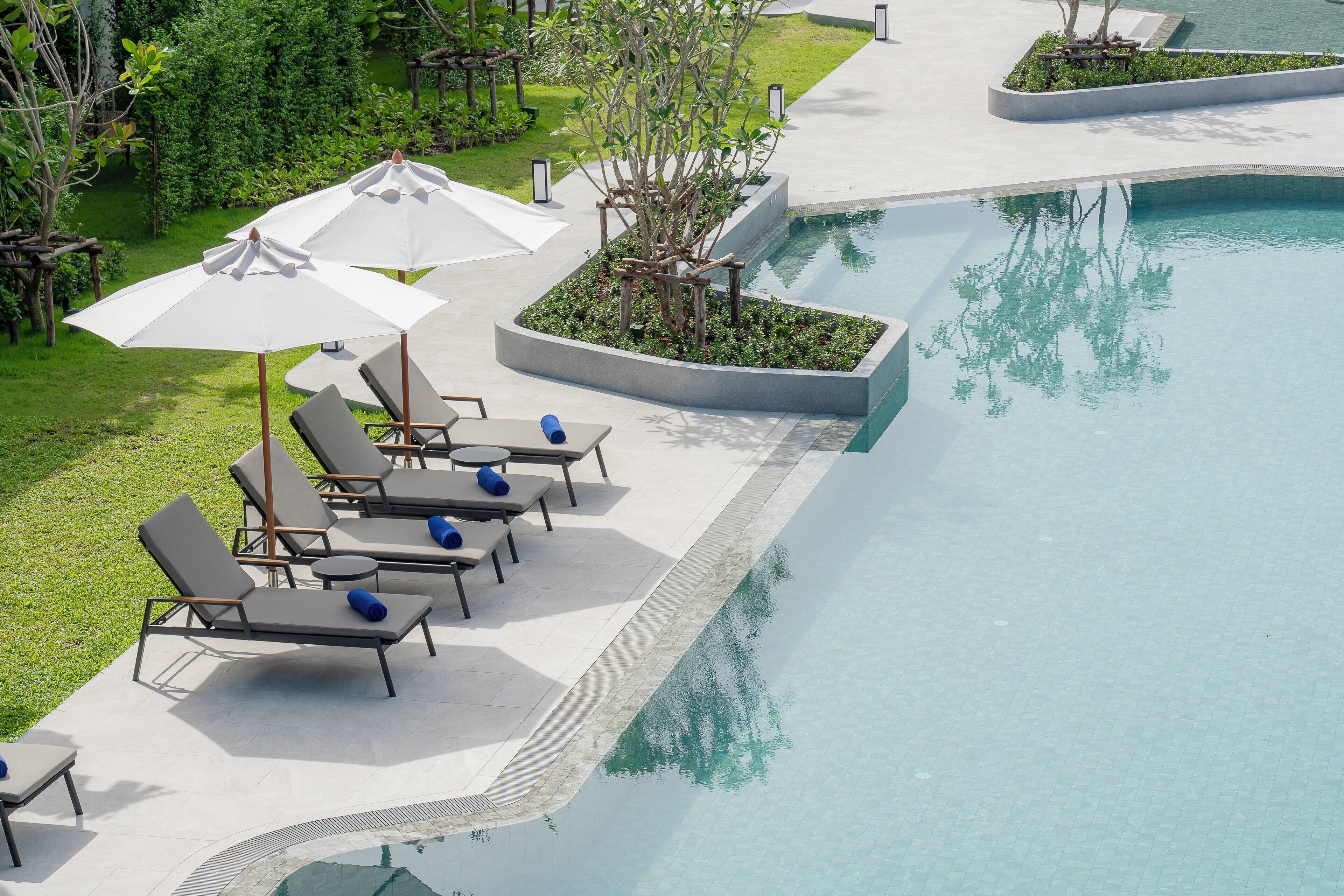 Zona junto a la piscina con sillones de descanso y sombrillas, rodeada de vegetación y una piscina cristalina.