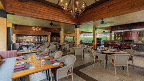 Un restaurant spacieux avec des plafonds en bois et plusieurs espaces de restauration. Les tables sont dressées avec des sets de table, des assiettes et des couverts.