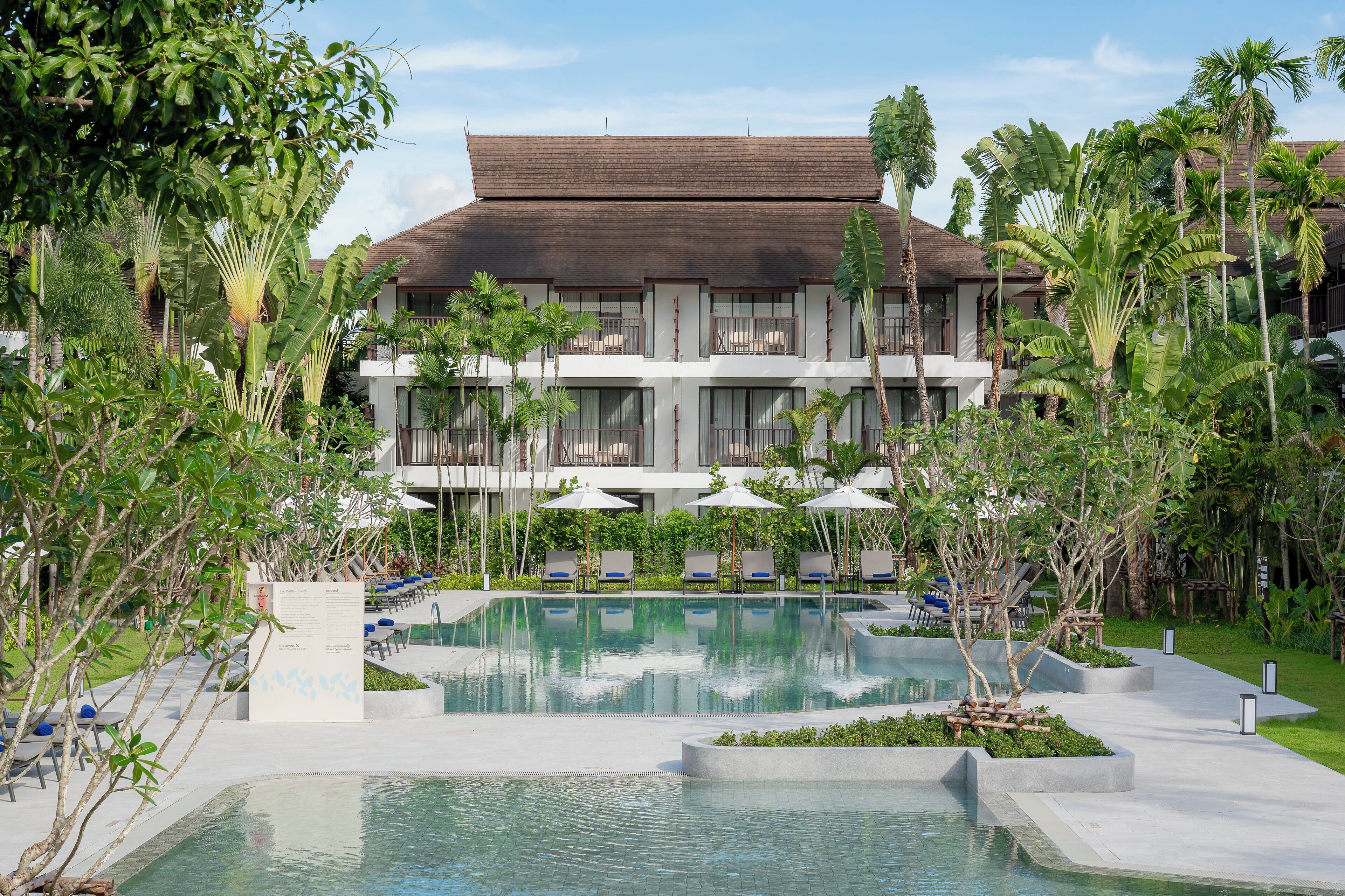 A resort with a large pool, lounge chairs, and tropical vegetation.